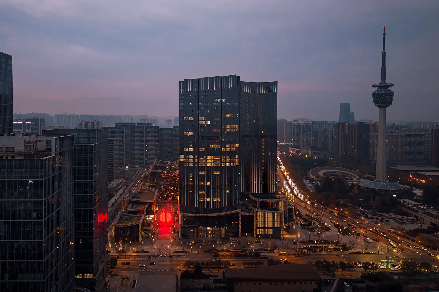 Wide aerial dusk view of SpY's DIVIDED red light installation glowing within the CCBD district of Xi'an, China, surrounded by modern skyscrapers and a television tower.