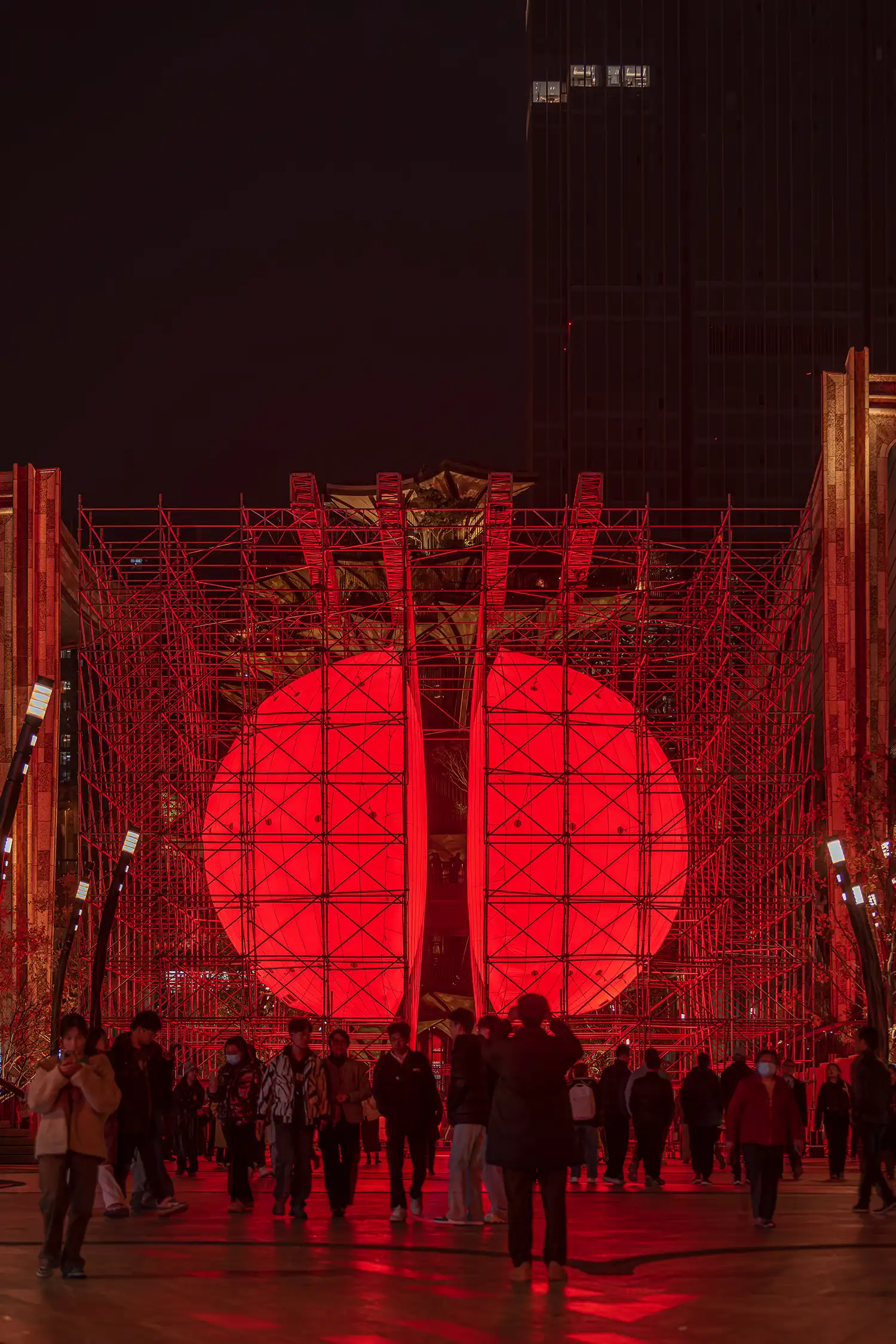 A group of people walking past the glowing red DIVIDED installation in a busy public plaza in Xi'an during the evening.