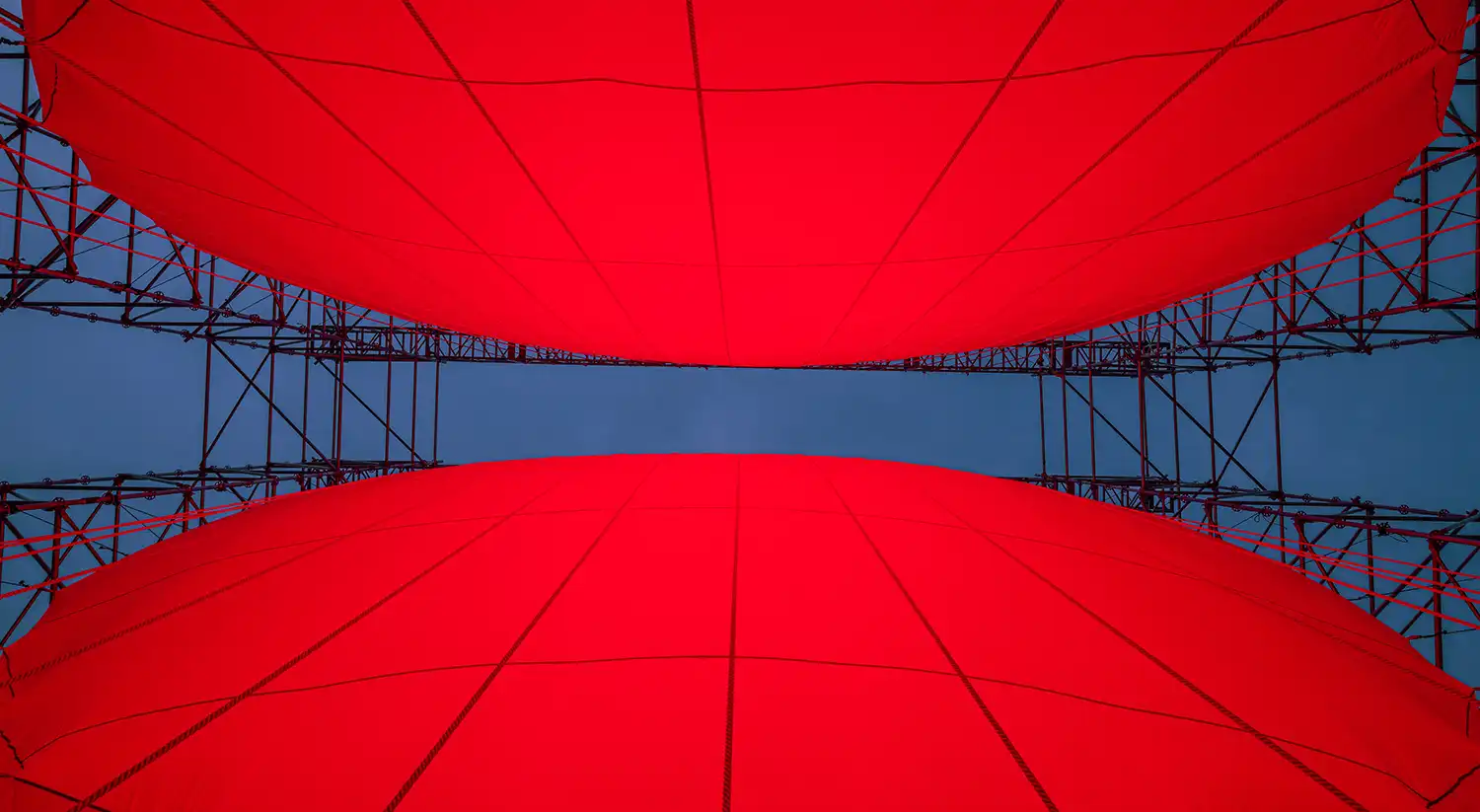 A vertical view from inside the corridor between the two red hemispheres of DIVIDED, looking up at the sky through the gap.