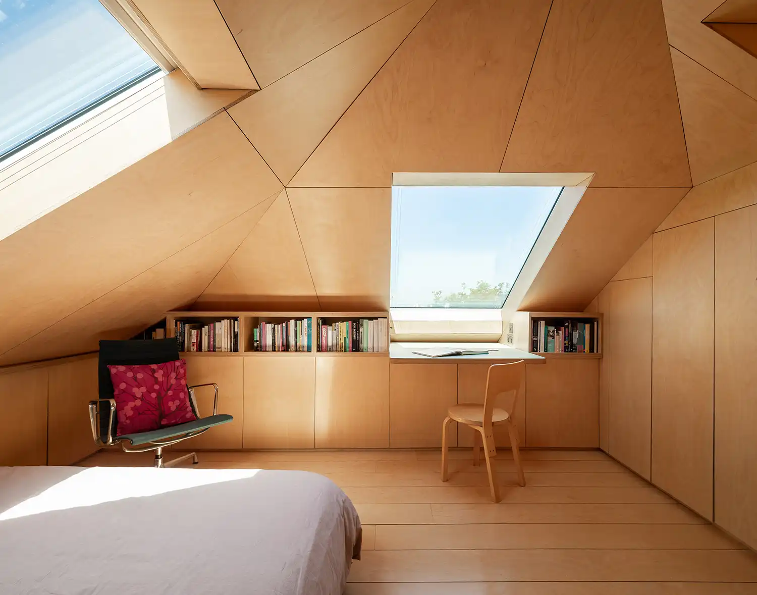 Minimalist attic bedroom with a built-in desk under a skylight and a reading chair.