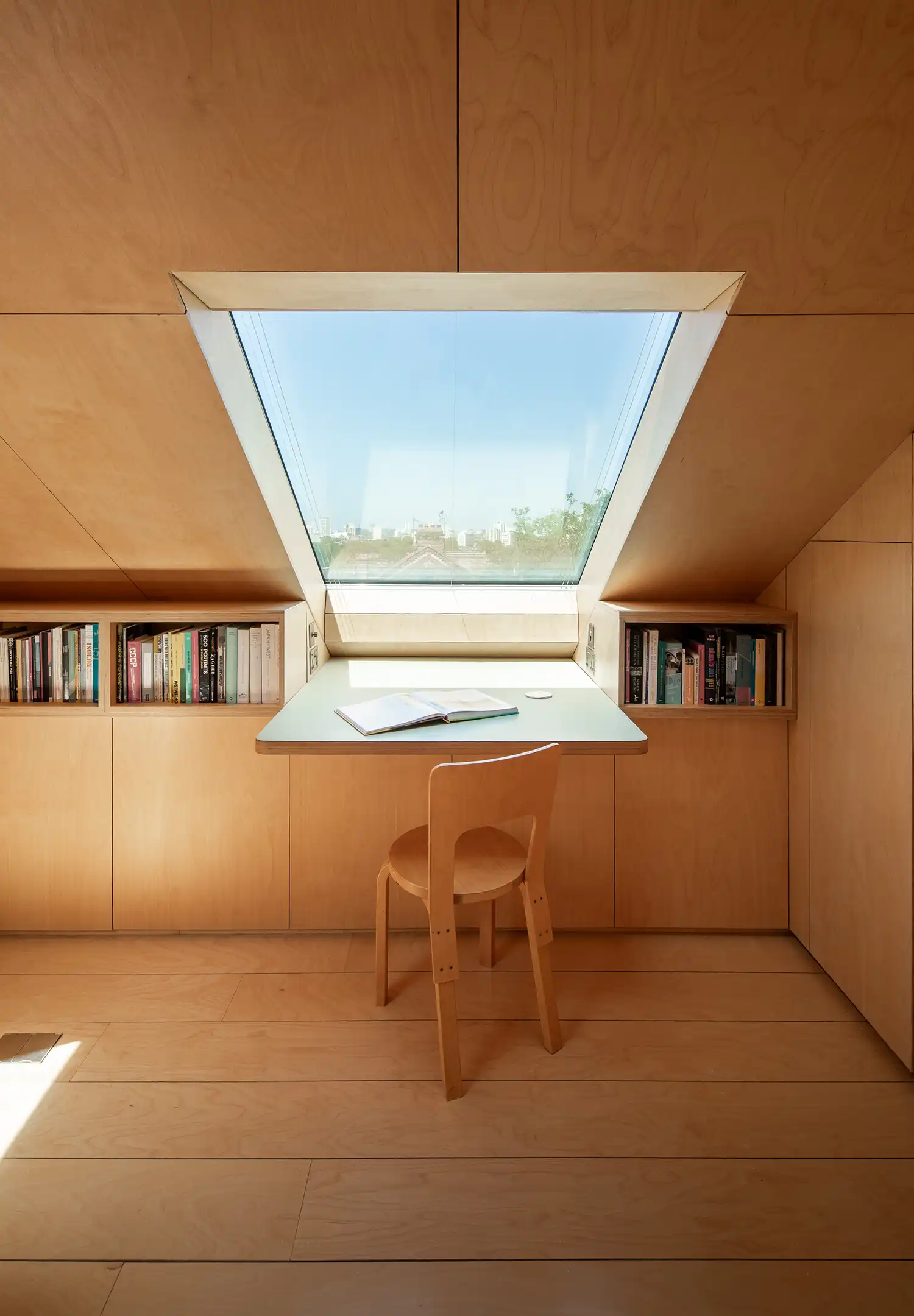 Centered view of a minimalist birch plywood desk positioned directly under a large skylight.