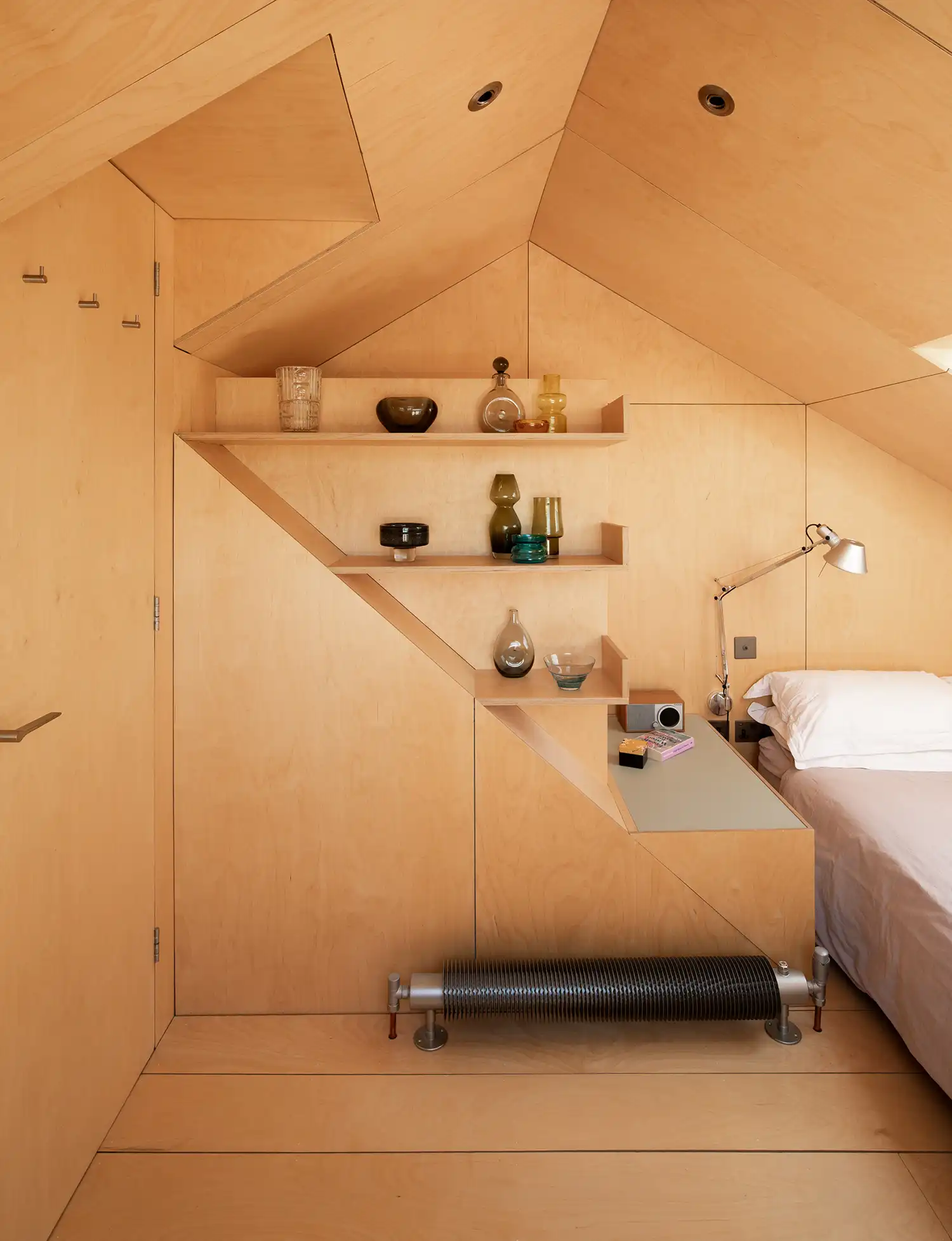 Detail of geometric birch plywood shelving and a floor-mounted industrial-style radiator.