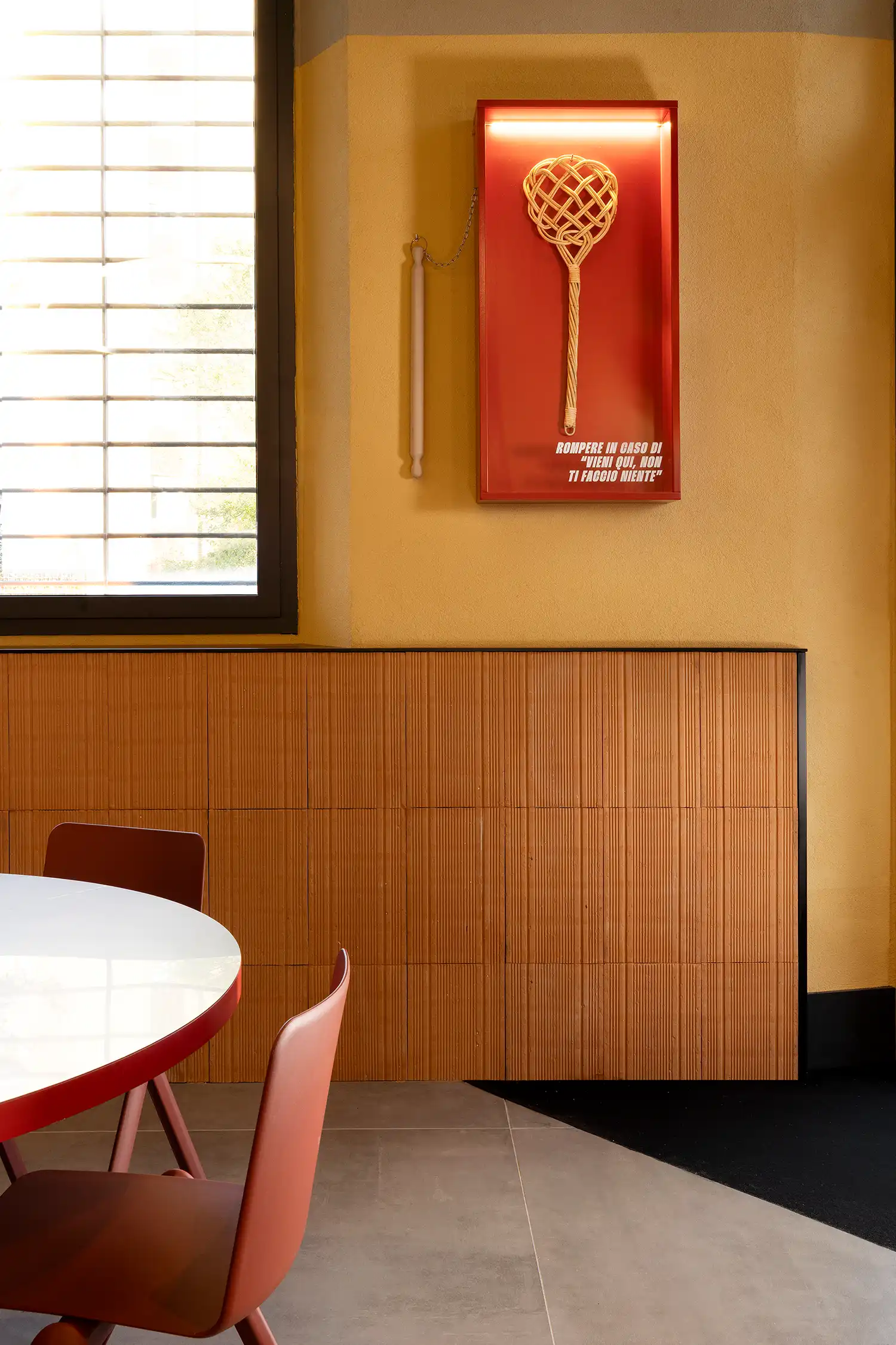 Close-up of a decorative red case with a woven whisk and Italian text on a yellow textured wall.