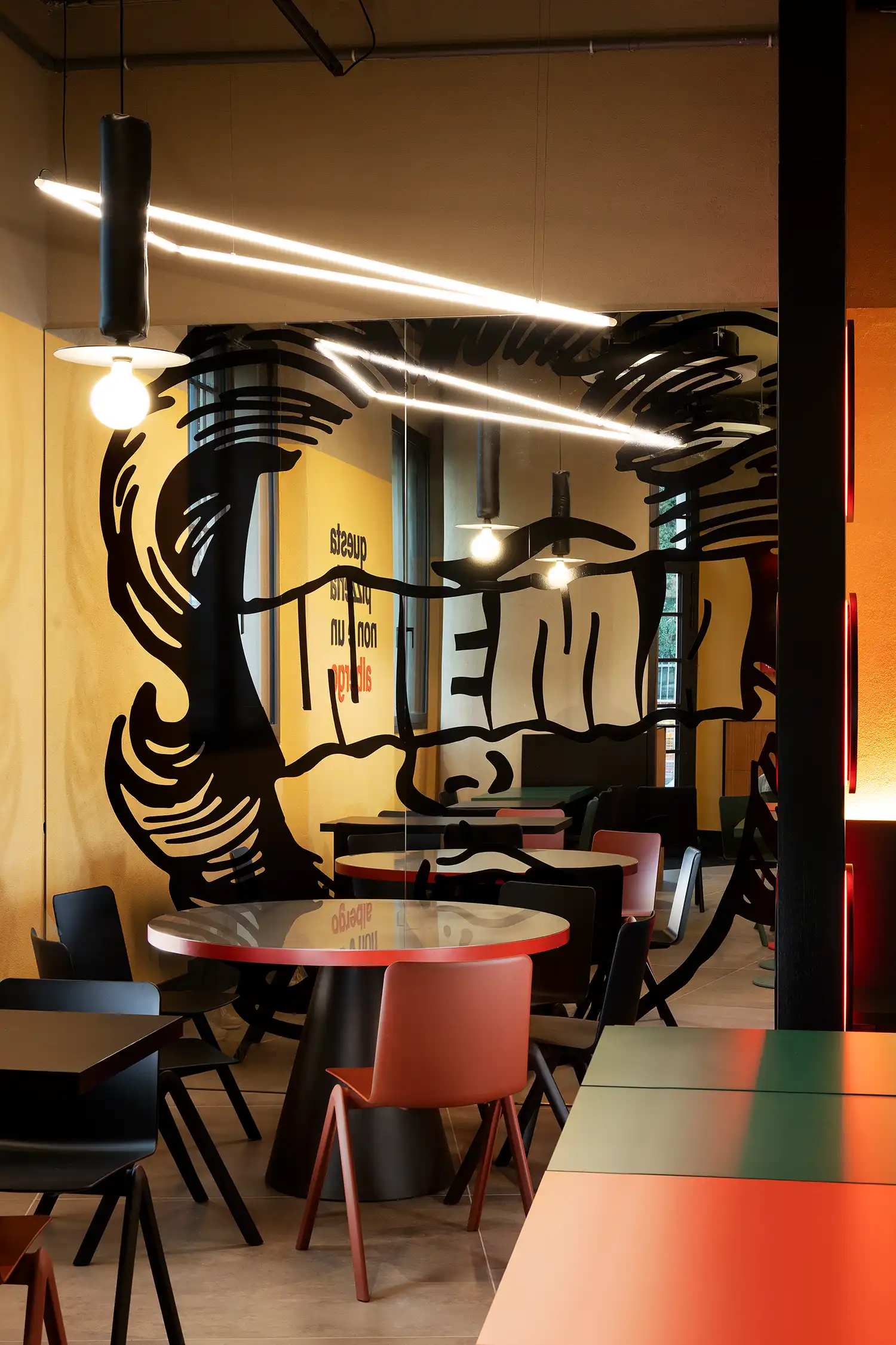 Mirrored wall in WÉMA restaurant reflecting pop-art graphics, pendant lights, and colorful dining chairs.