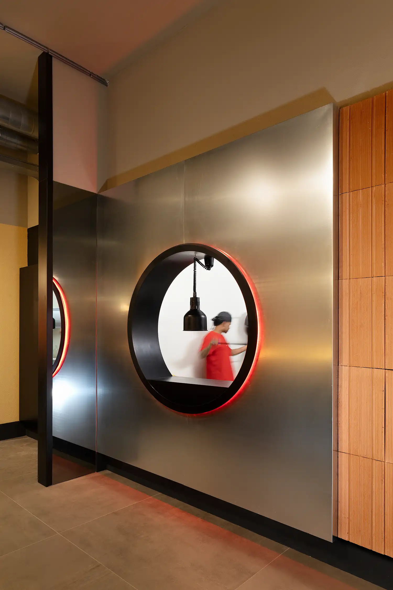 Stainless steel kitchen pass with a circular porthole window and red LED halo at WÉMA Milan.