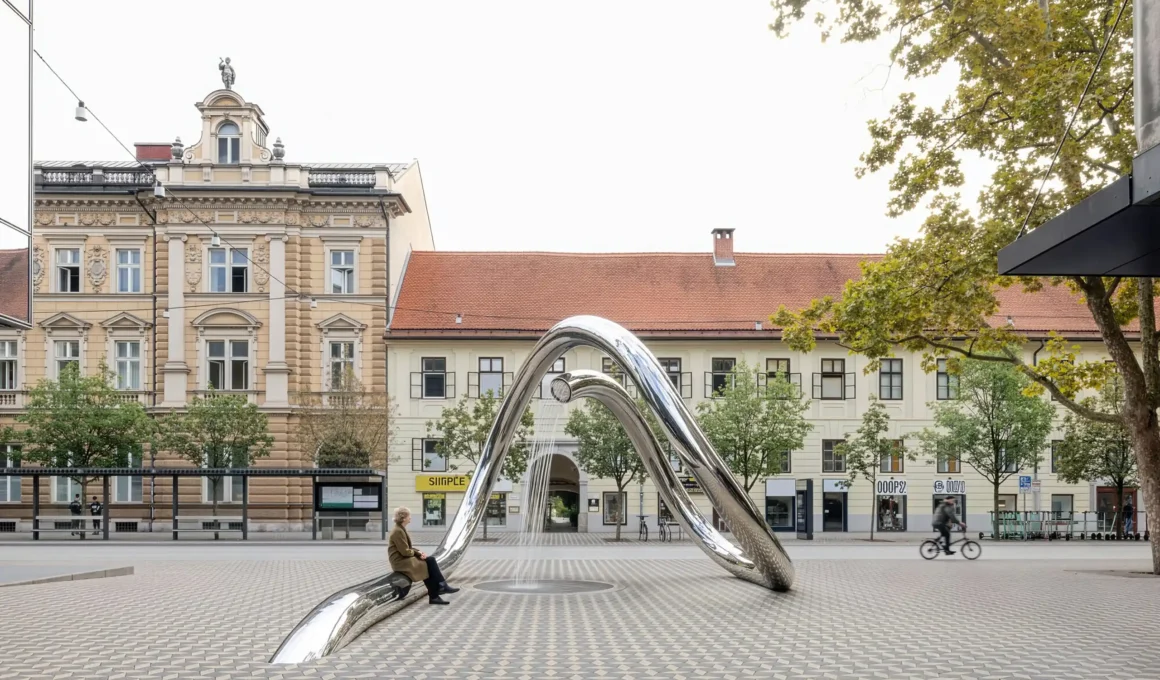 Person sitting on the base of a looping stainless steel water sculpture in Ljubljana.