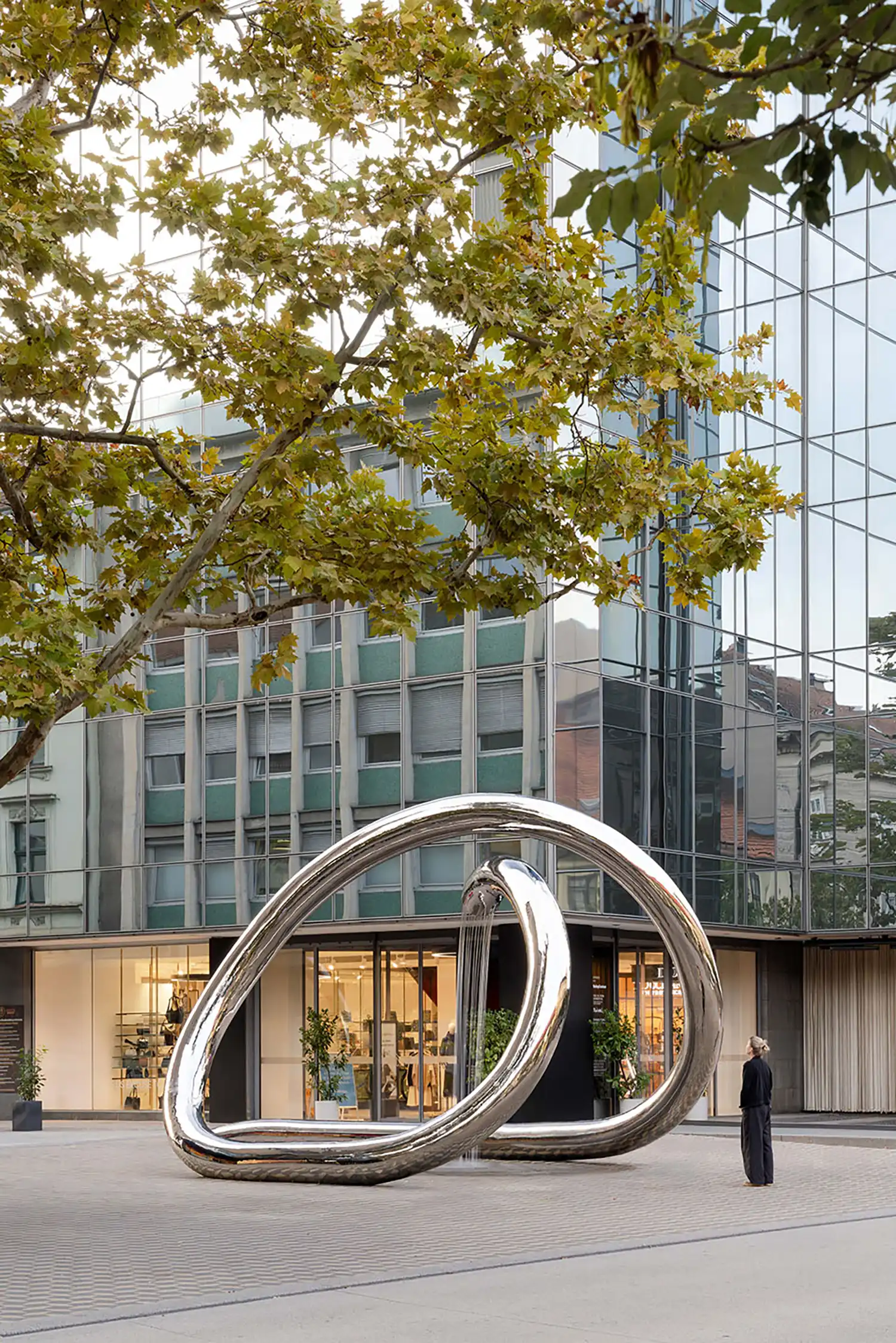 Modern stainless steel sculpture framing a pedestrian street and a lone figure.