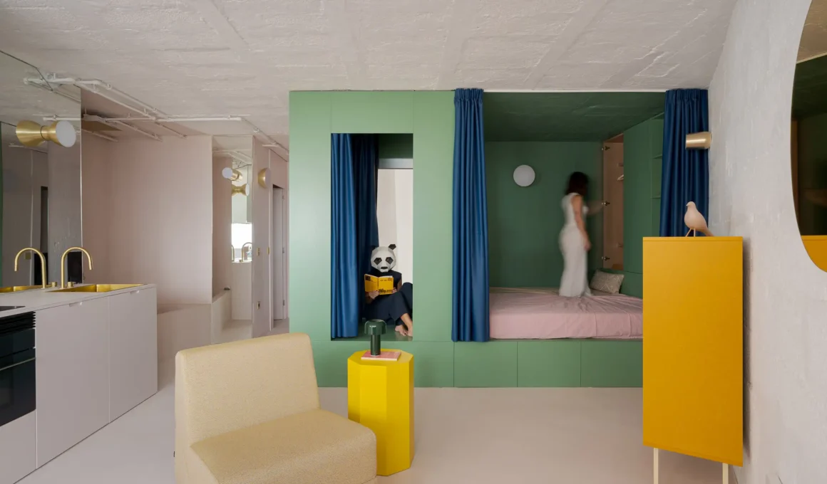 View of the green sleeping volume in House C featuring a person in a panda mask reading in the niche.