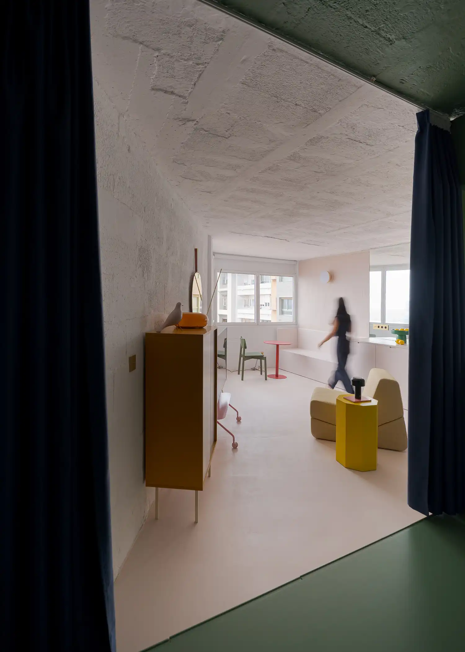Long perspective view of House C from the entrance toward the window, showing yellow furniture accents.