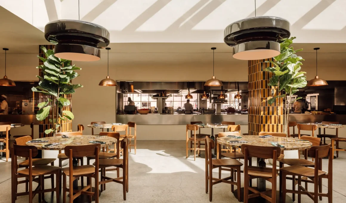 Main dining hall of Zero Zero Belém with sunlight streaming from above onto stone tables and walnut chairs.