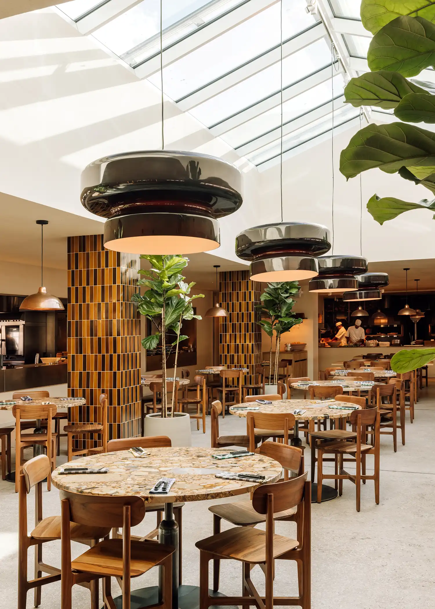 Vertical view of the dining area beneath a large glass skylight featuring black sculptural pendant lamps.