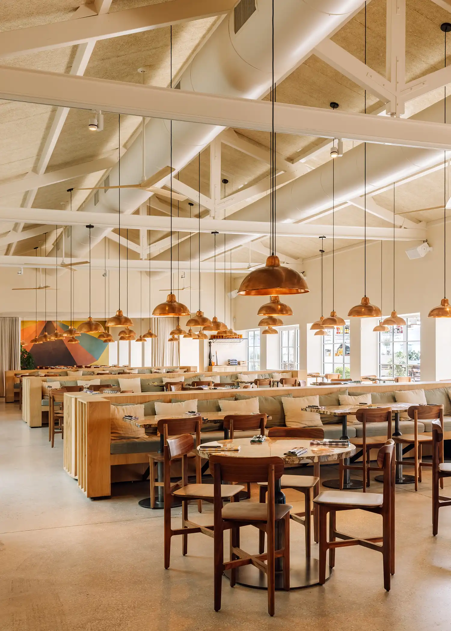 Interior view of a long dining hall with rows of booths, copper lamps, and a colorful mural in the distance.