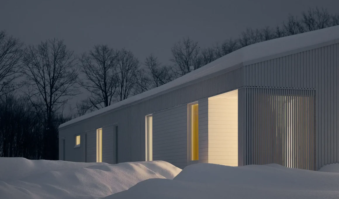 Close-up of white board-and-batten cladding and slatted wood screen at night in the snow.
