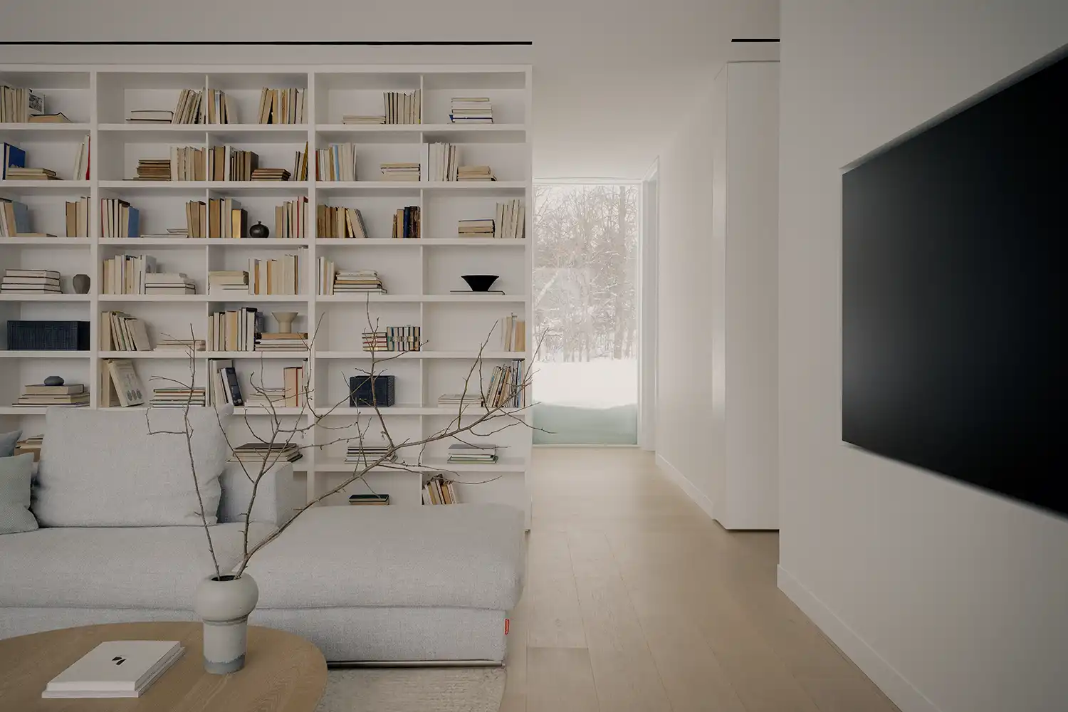 Modern living room with a recessed television screen and large white bookshelf.