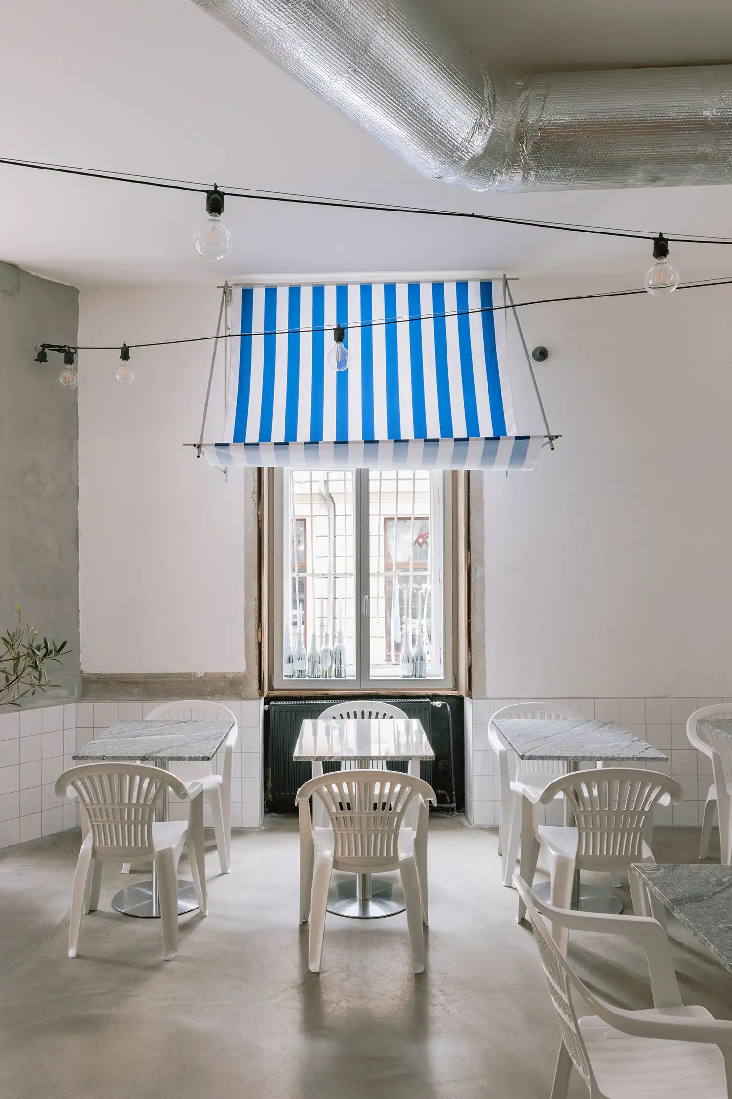 Minimalist window niche in a Bratislava restaurant with a blue striped awning and marble table.