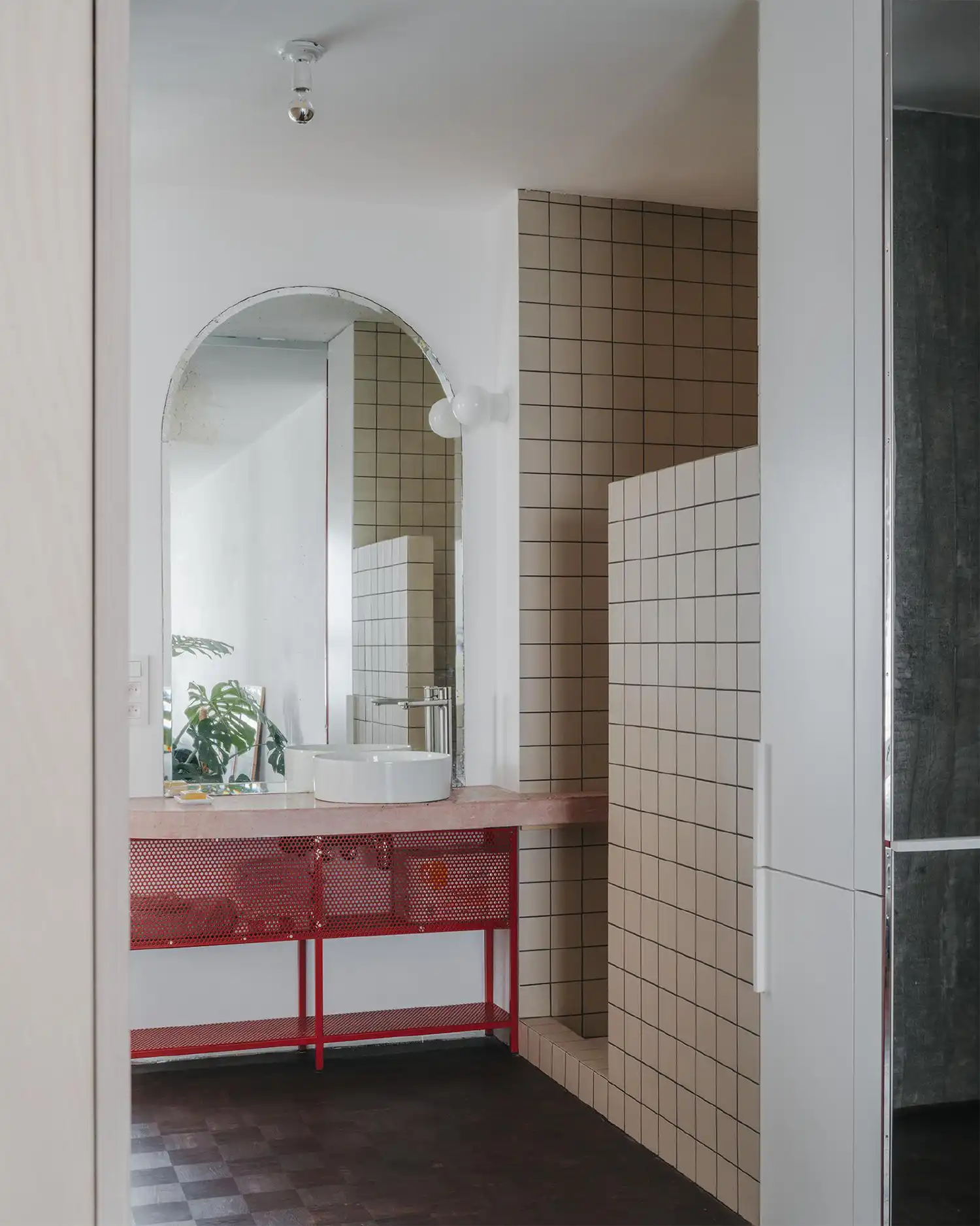 Open bathroom corner with arched mirror, white tiled shower, and red mesh vanity base.