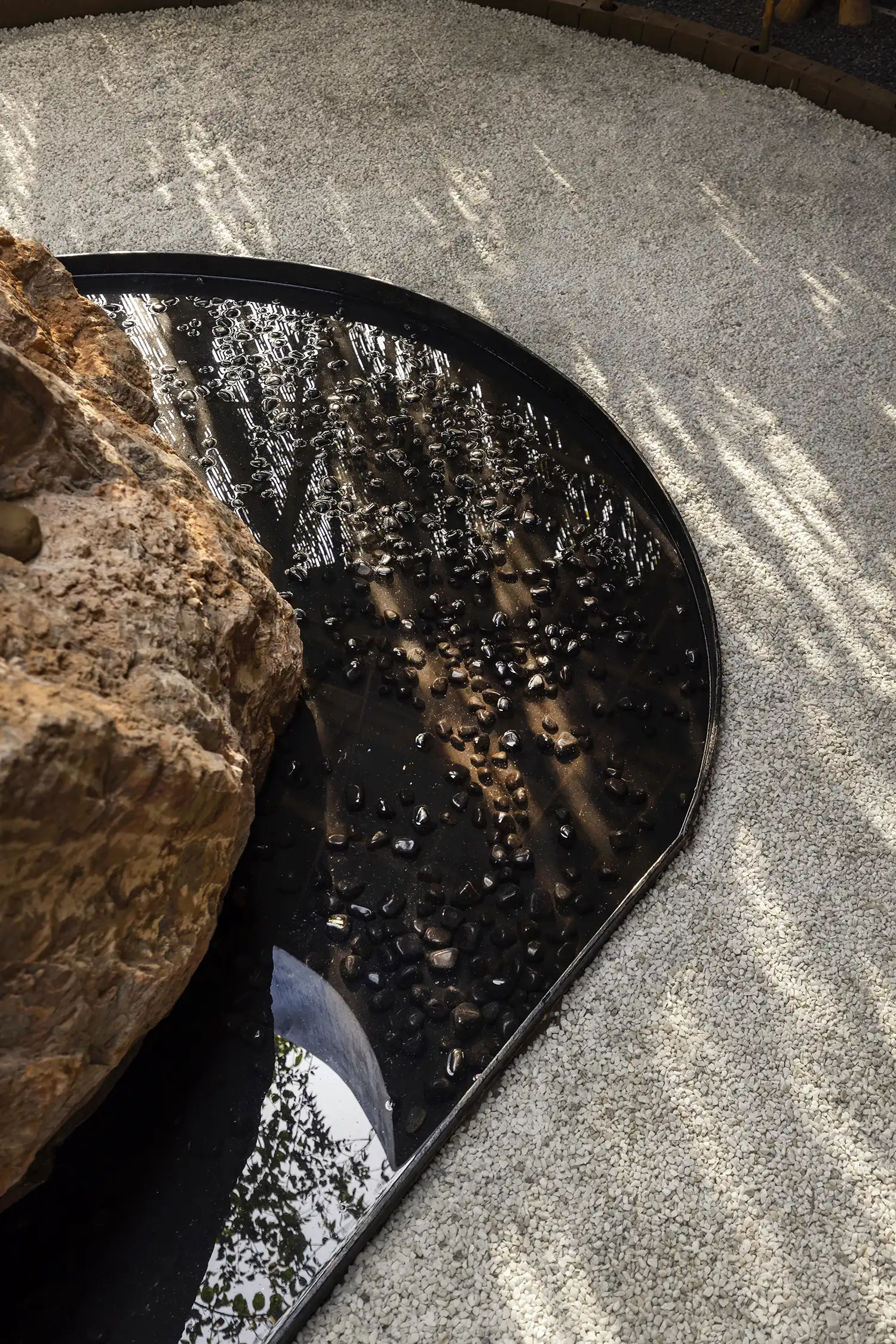 Close-up of a stone centerpiece in a shallow dark water pool surrounded by white pebbles.