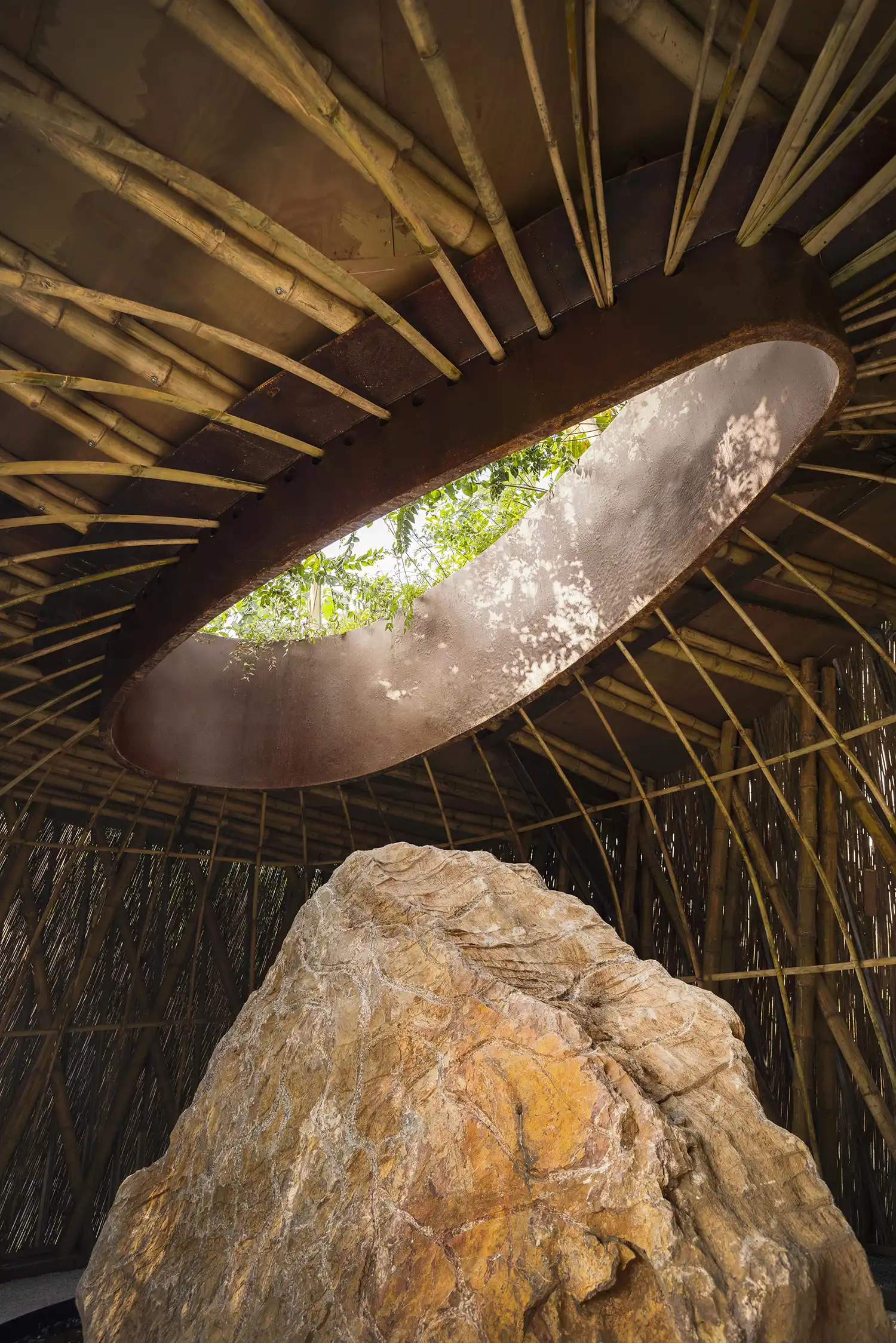 A vertical view of an oval oculus in the bamboo ceiling revealing green foliage above.