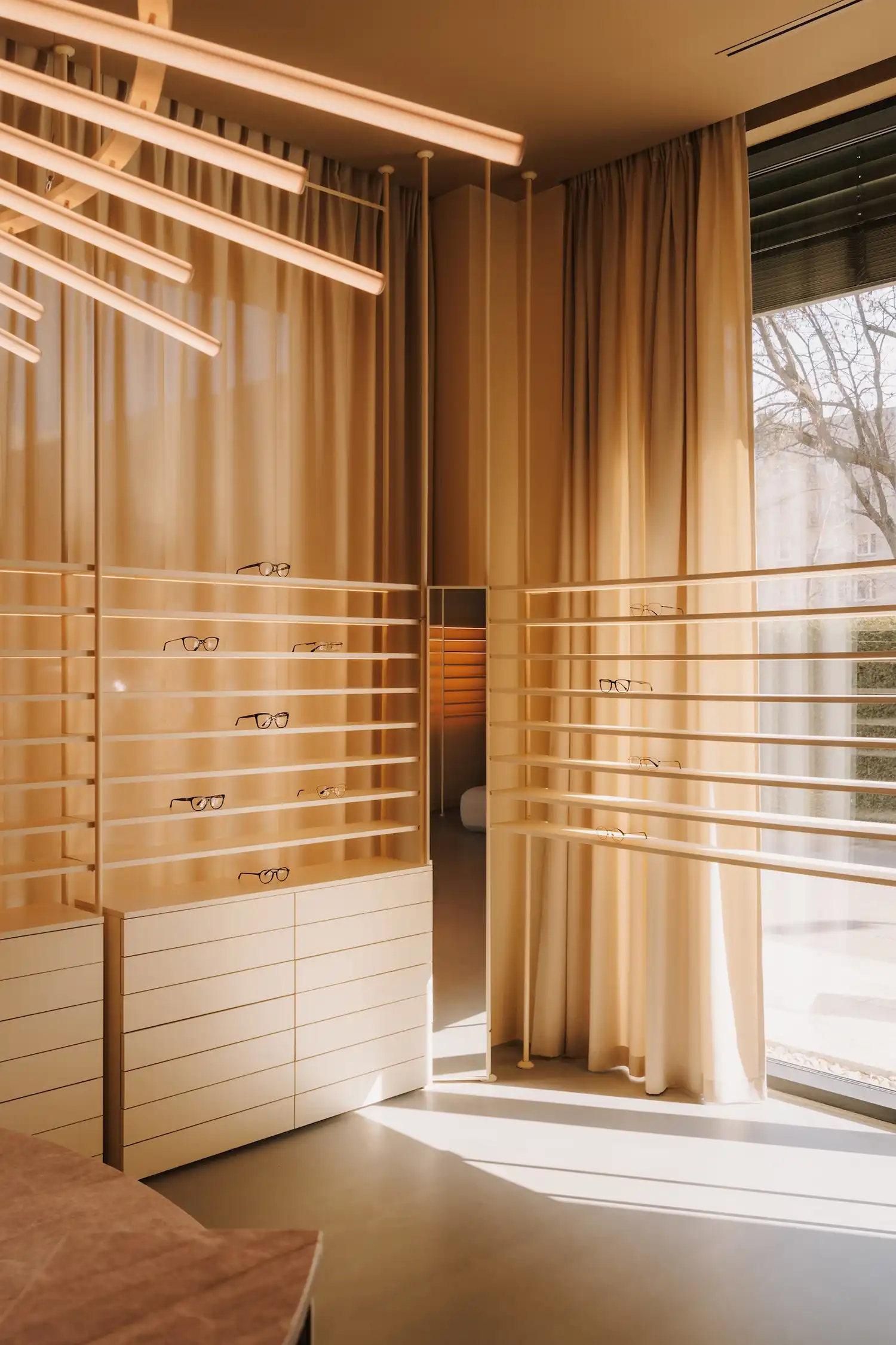 Minimalist eyewear display shelving with warm backlighting and soft curtains.