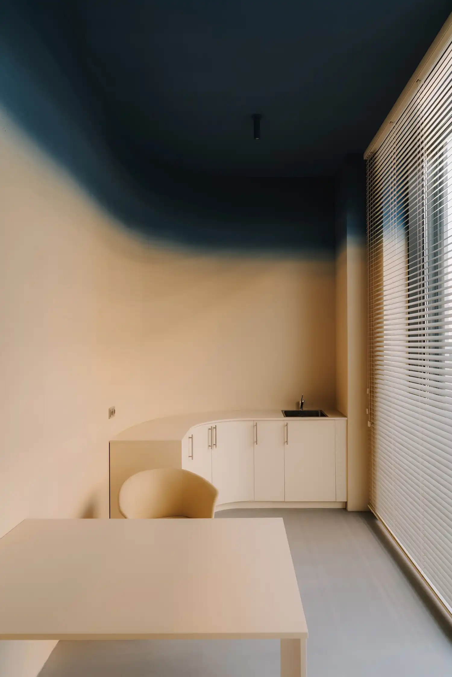 Examination room with a blue-to-beige gradient wall and minimalist white cabinetry.