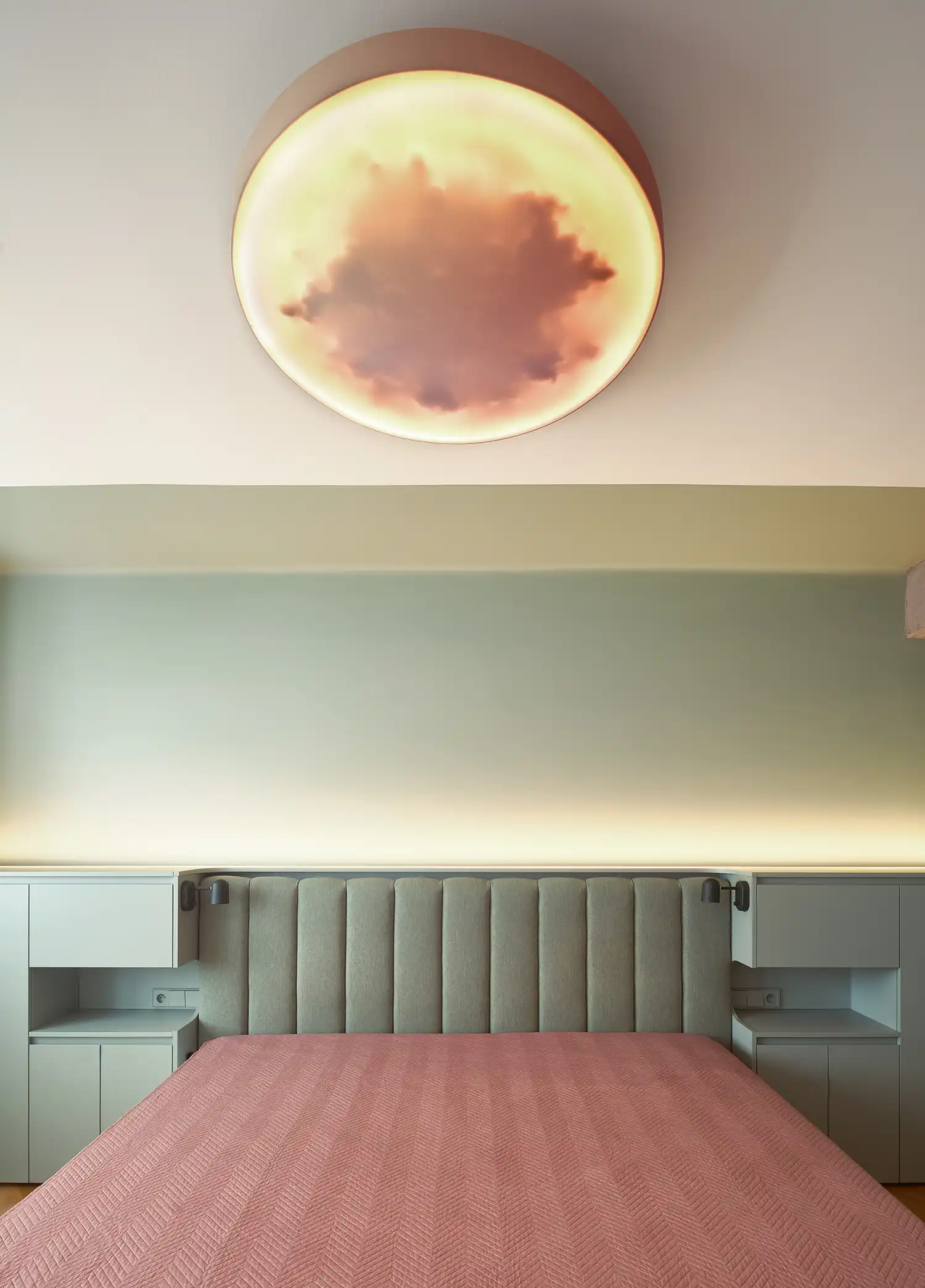 Modern bedroom with a sage green wall, ribbed headboard, and a cloud-patterned circular ceiling light.