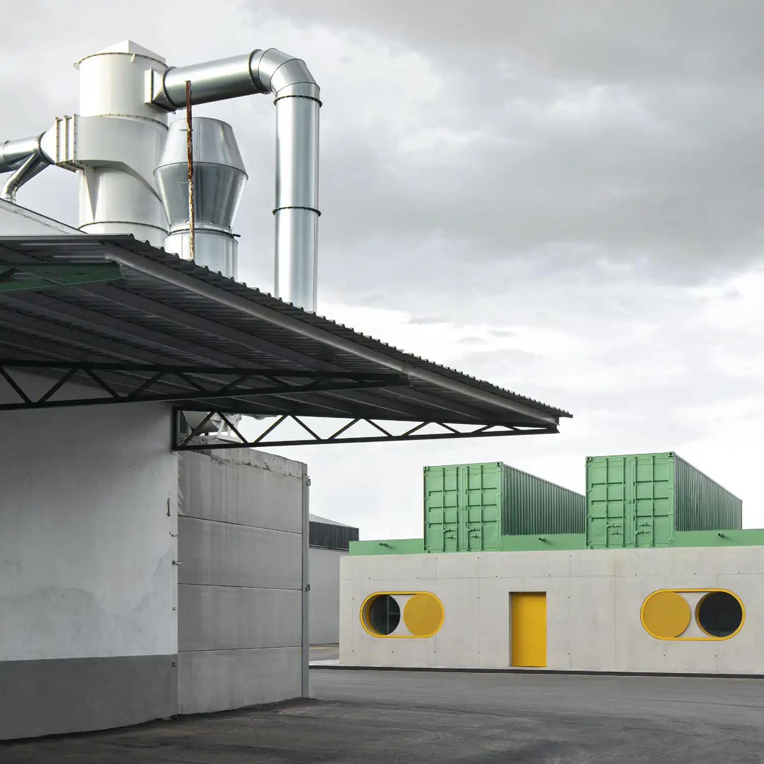 Repurposed green shipping containers atop a concrete office with circular yellow shutters