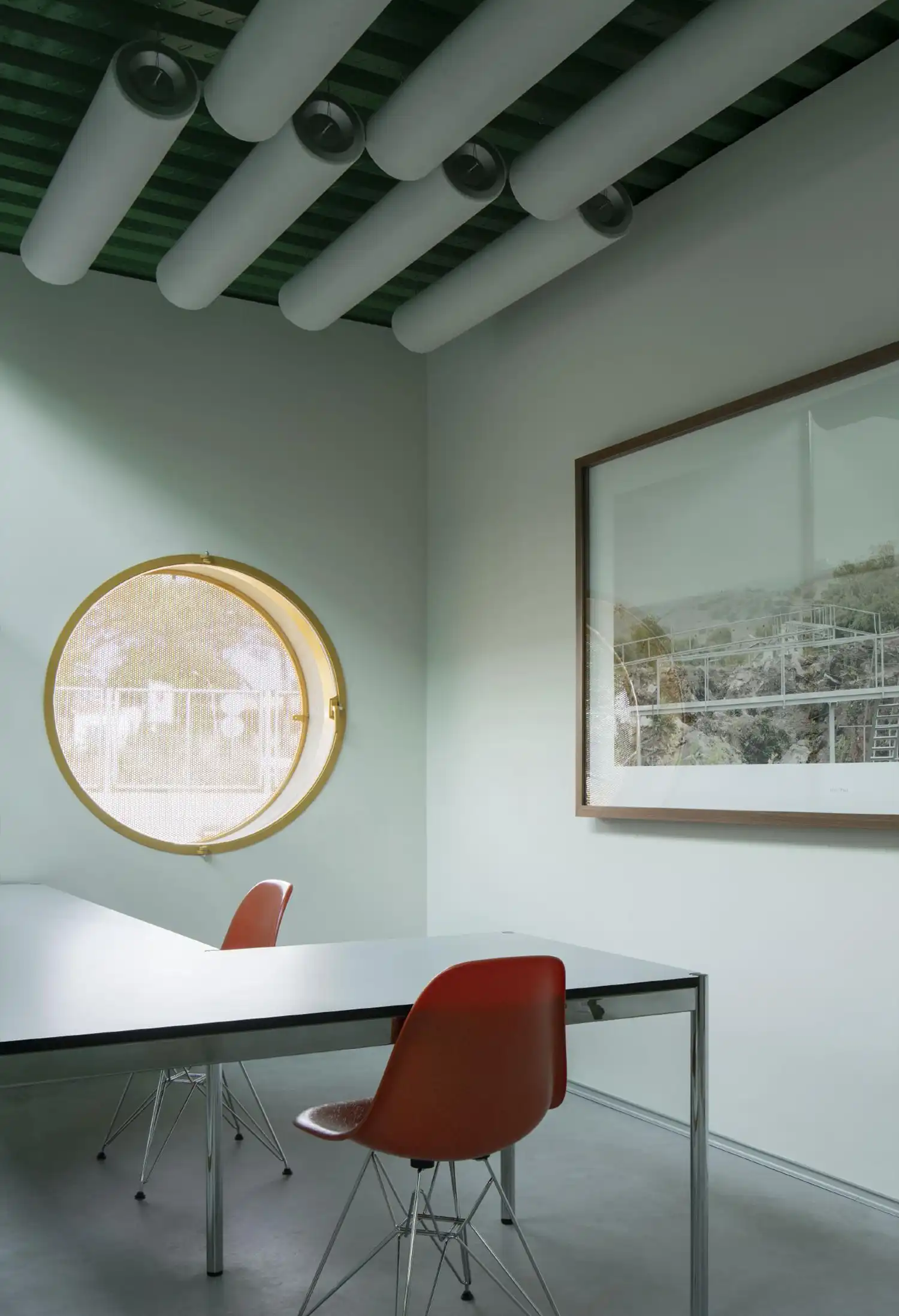 Circular window detail in a minimalist meeting room with red chairs