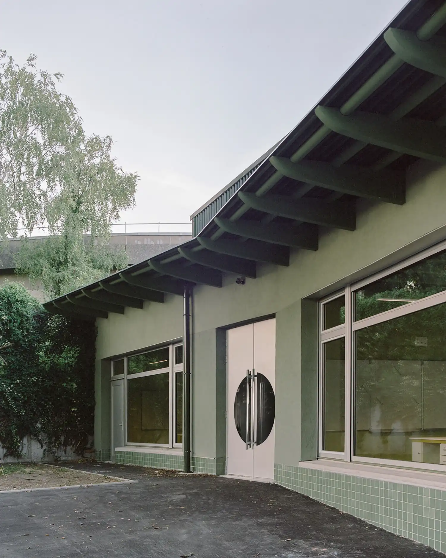 Close-up of the school entrance with white double doors featuring circular glass windows, under a green roof overhang.