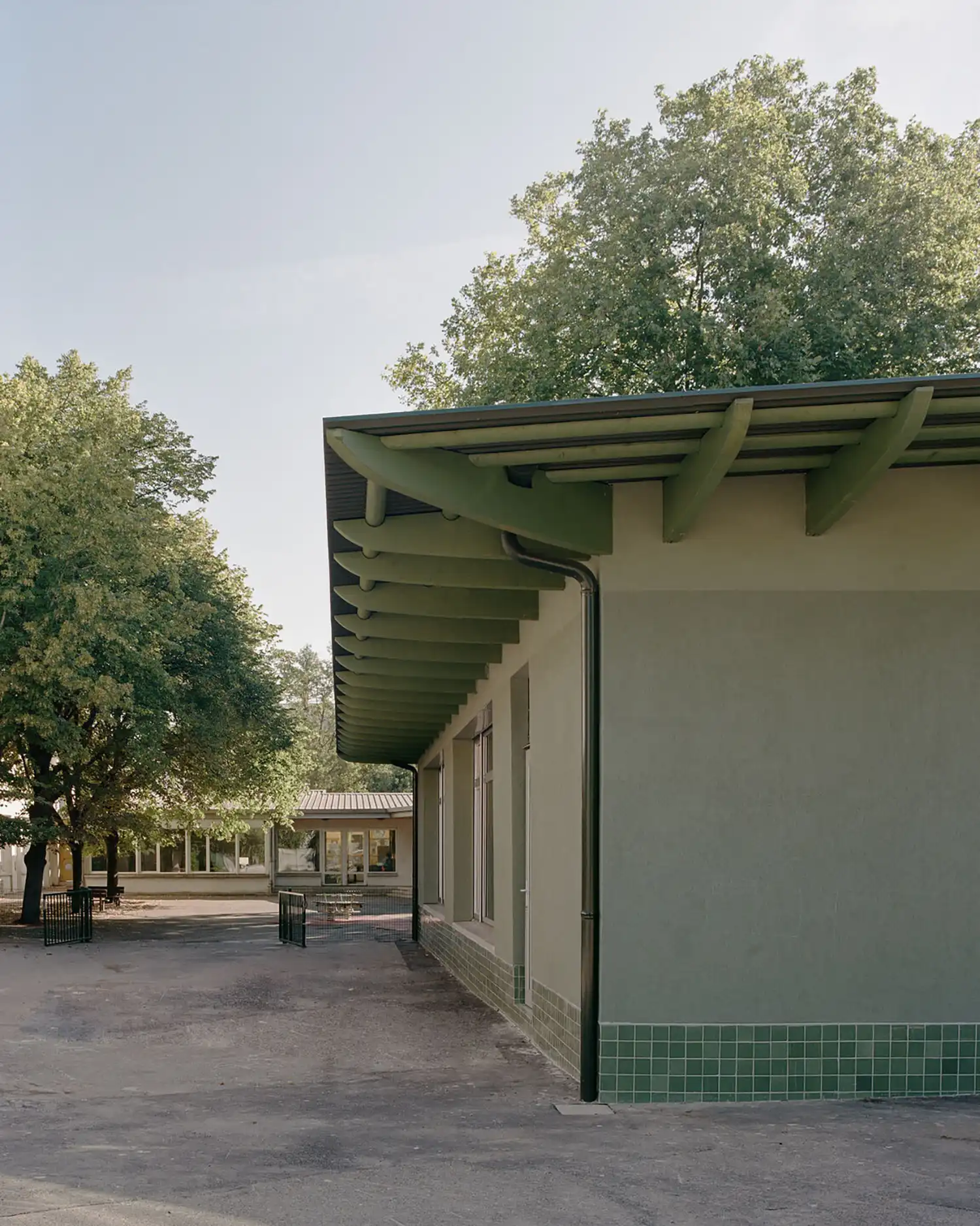 Exterior angle showing the corner of the green school building, emphasizing the green roof beams and the tiled base.