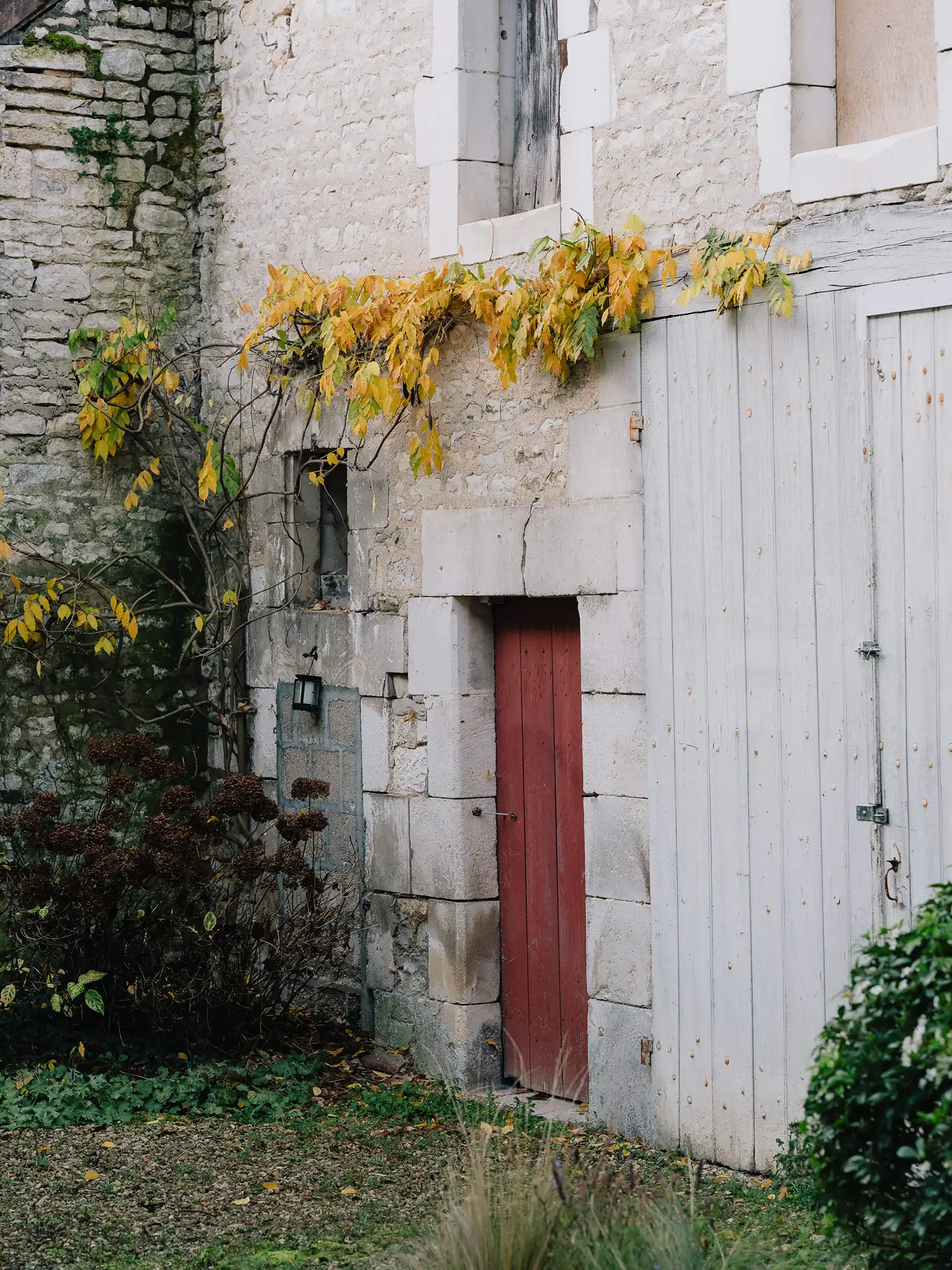 Historic stone exterior of a French winemaker cottage with a red door and climbing vines.