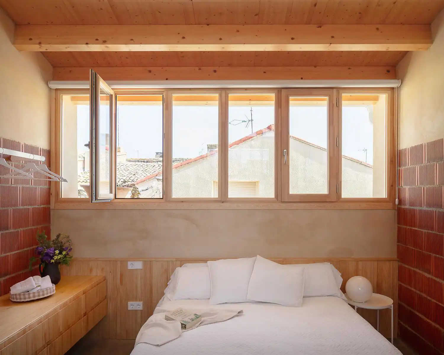 Minimalist bedroom in Casa Felipa with a large window and timber-beamed ceiling.