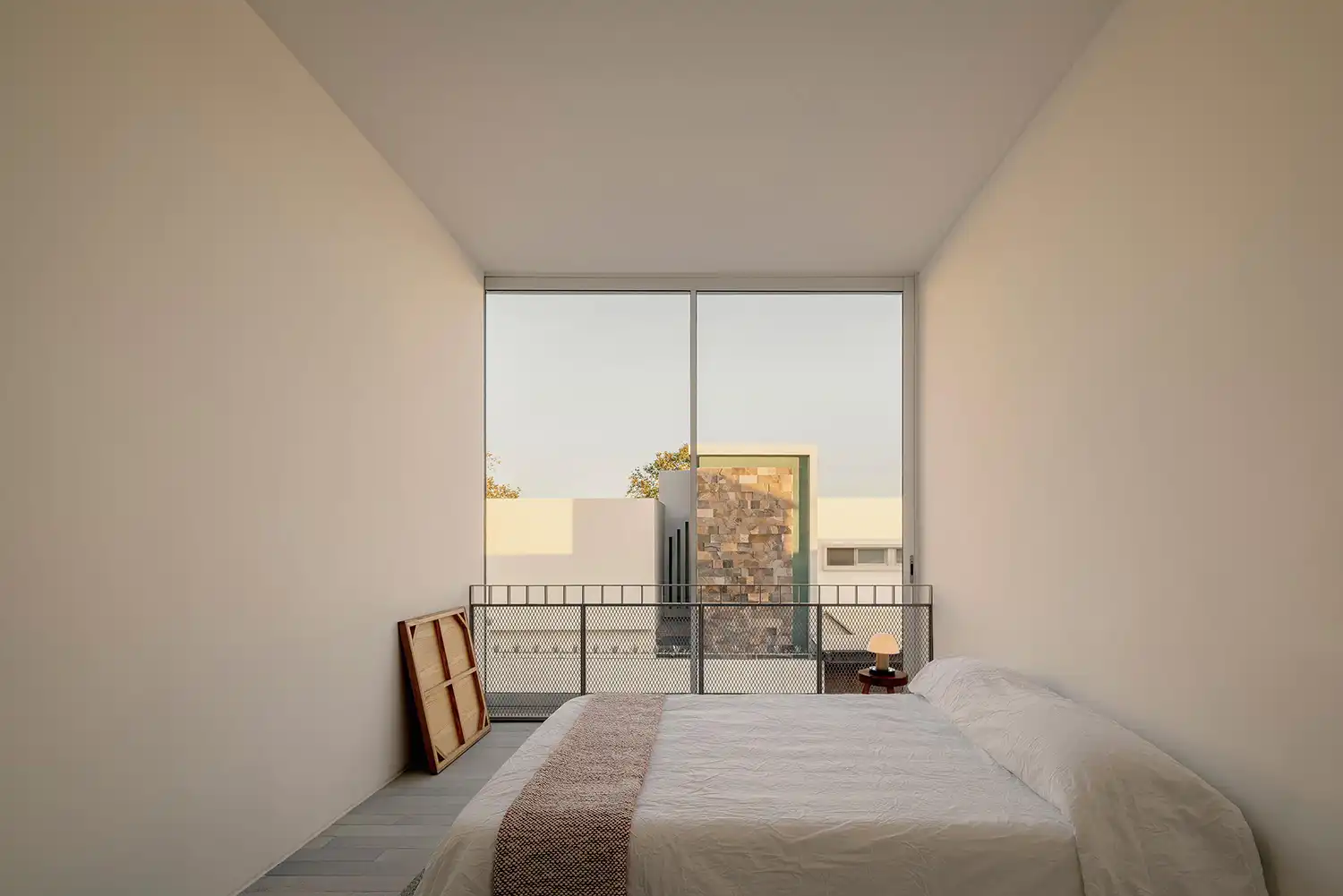 Stark white bedroom with a floor-to-ceiling window overlooking urban rooftops.