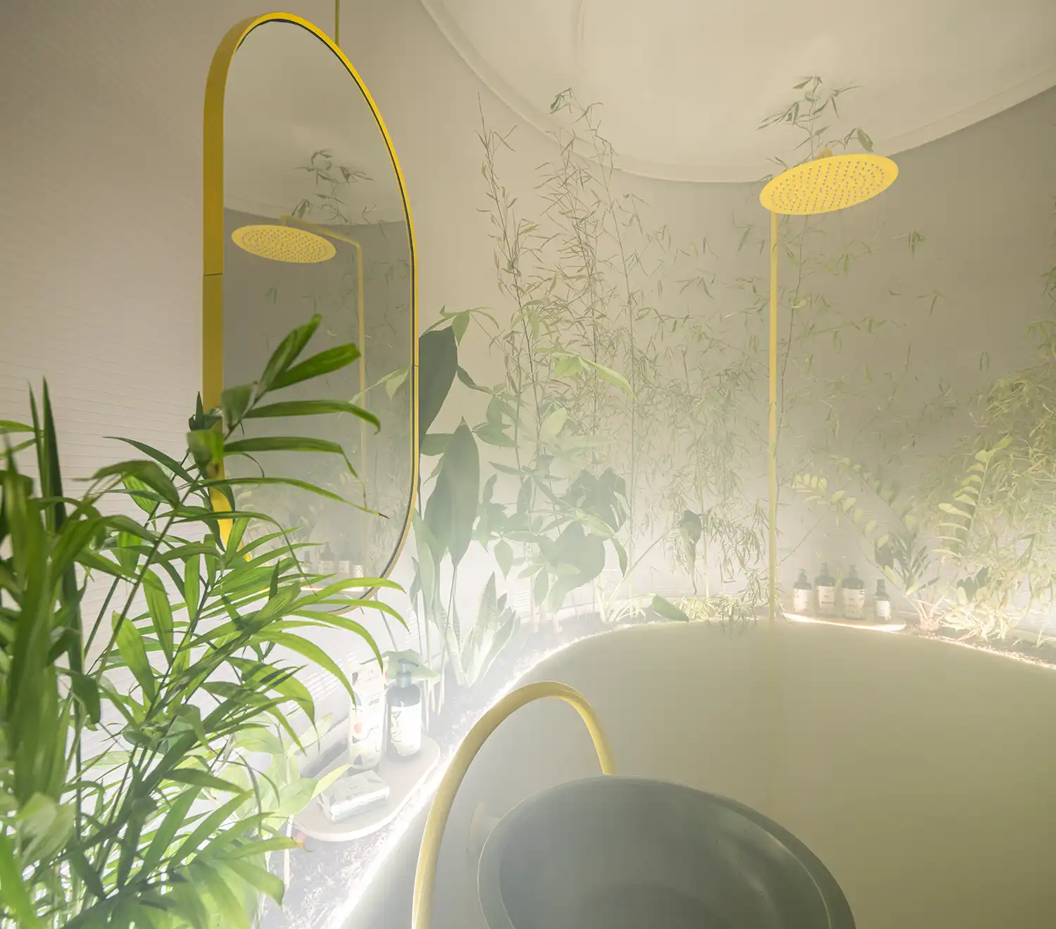 Interior of a circular bathroom with bamboo plants, a yellow showerhead, and an oval mirror.