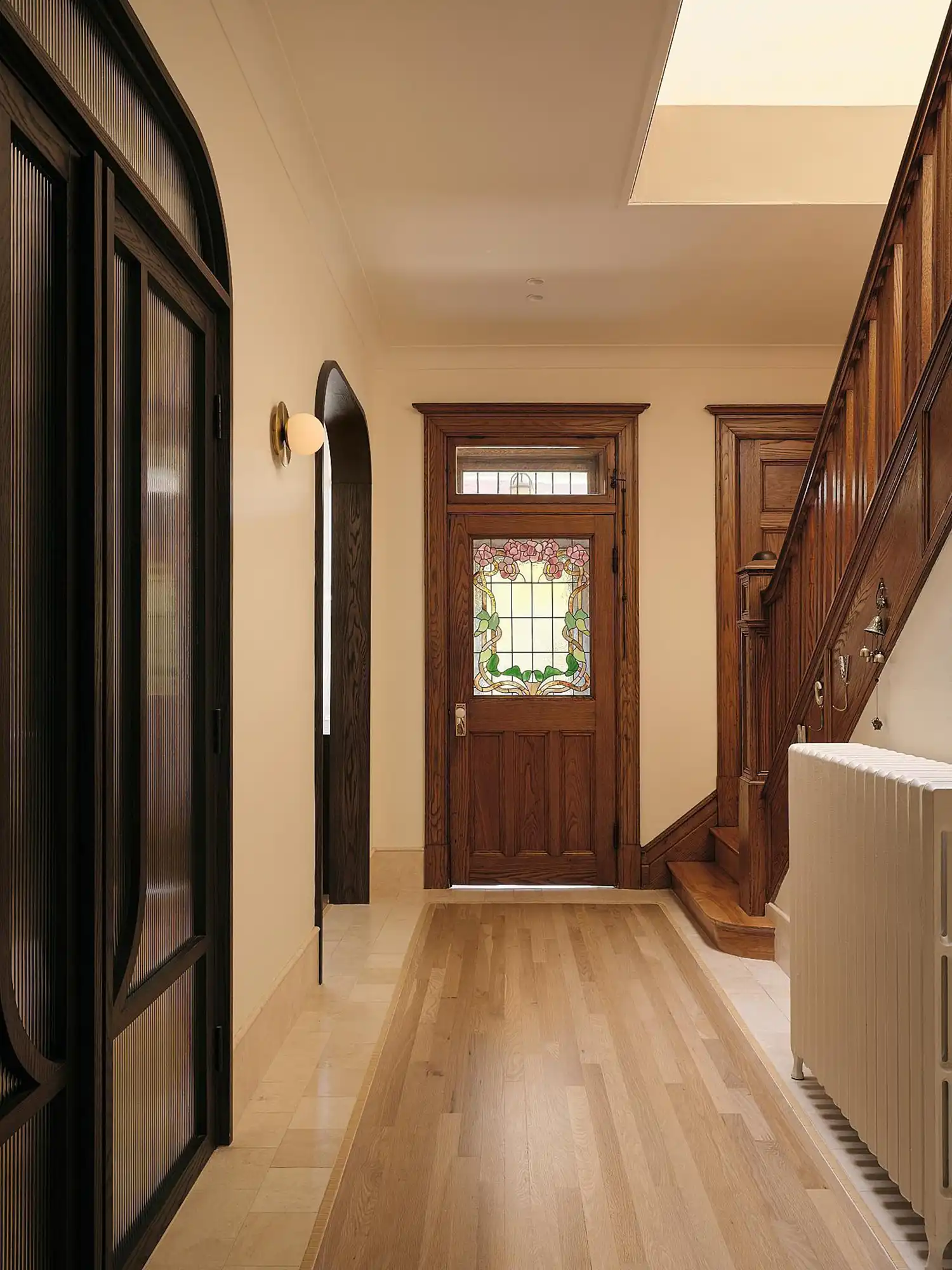 The preserved central staircase and stained-glass door act as anchors of memory within the contemporary renovation.