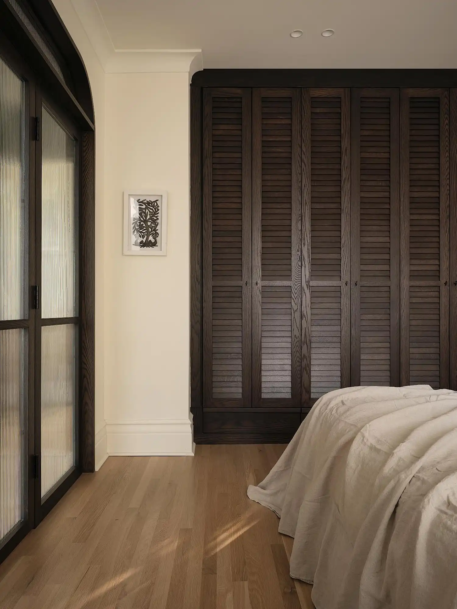Custom louvered wardrobes and fluted glass doors define the calm, artisanal language of the primary suite.