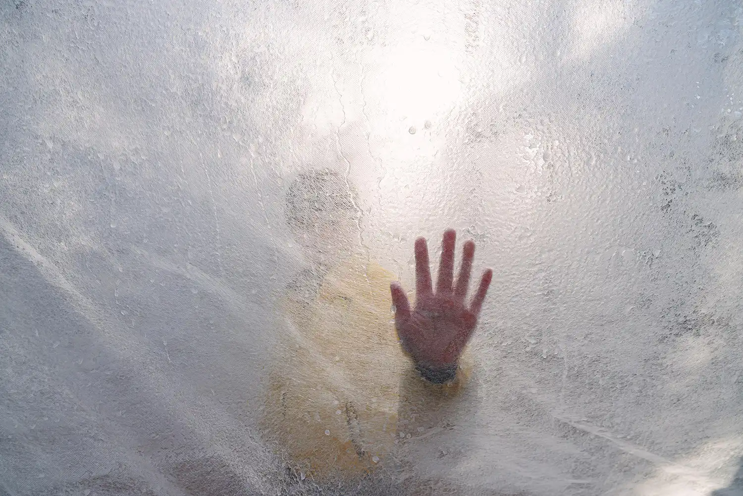A close-up, backlit view of a hand pressed against a textured, semi-transparent ice surface.