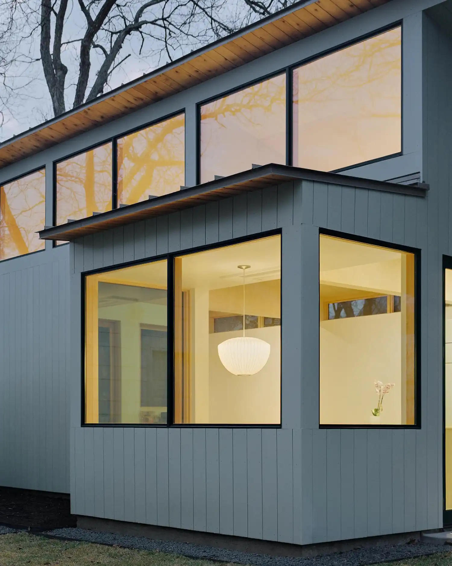 Exterior detail of a projected glass corner window showing a lit interior pendant.