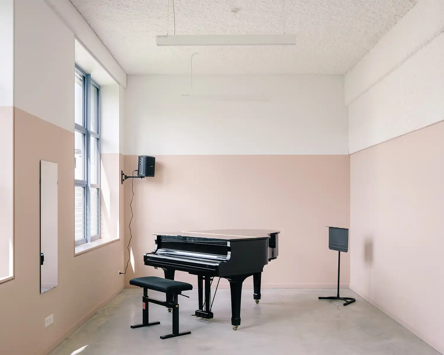 A grand piano in a music rehearsal room with a two-tone pink and white wall.