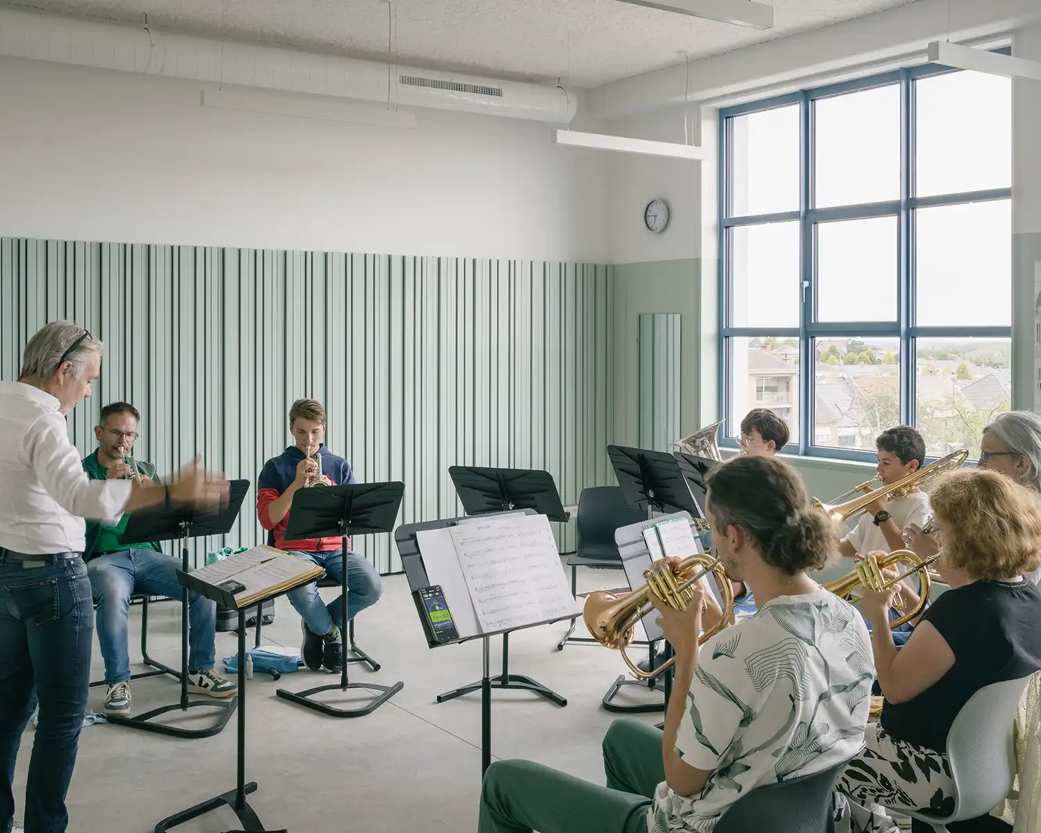 A brass ensemble rehearsing in a studio with light green acoustic wall panels.