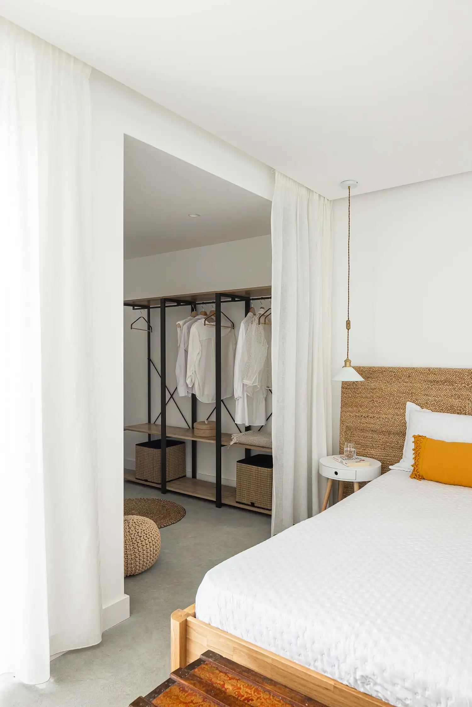 Minimalist white bedroom with open wooden wardrobe and straw headboard