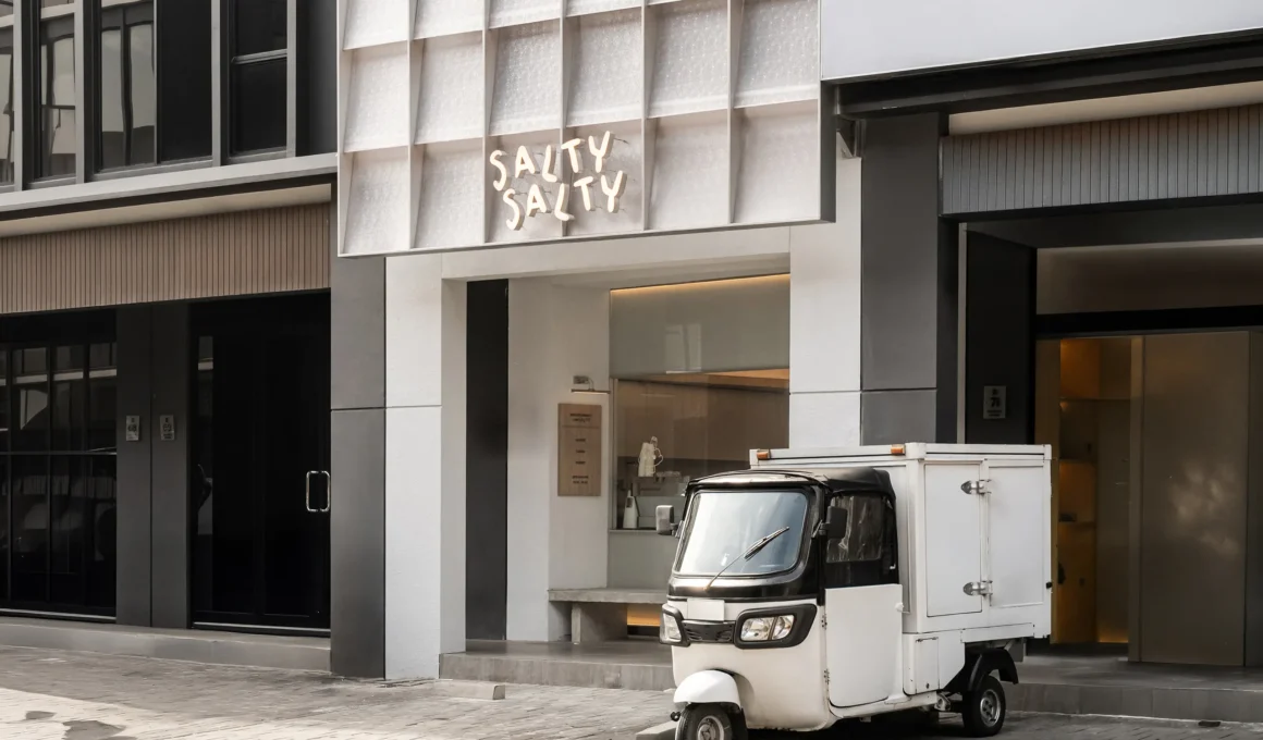 Wide view of Salty Salty cafe's white grid facade with a delivery tricycle parked in front.