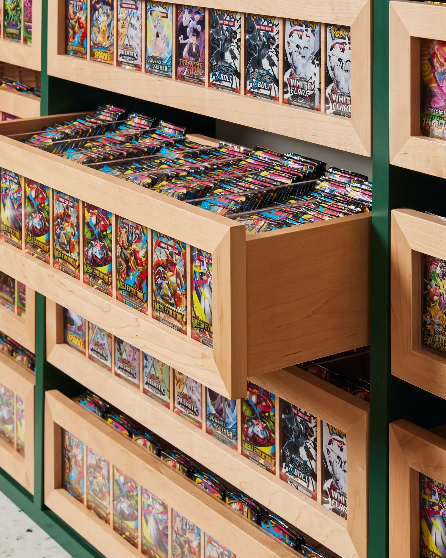 Close-up of open maple wood drawers filled with organized Pokémon trading card packs.