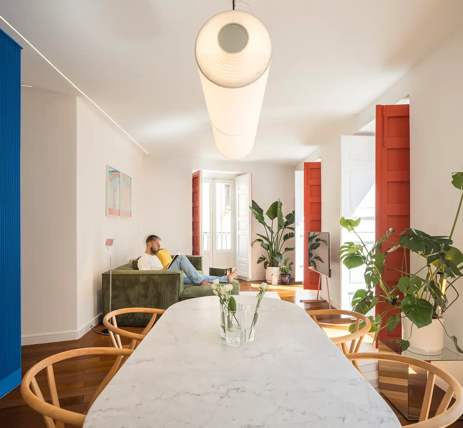 Open-plan living room with green sofa, marble table, and red shutters in Madrid