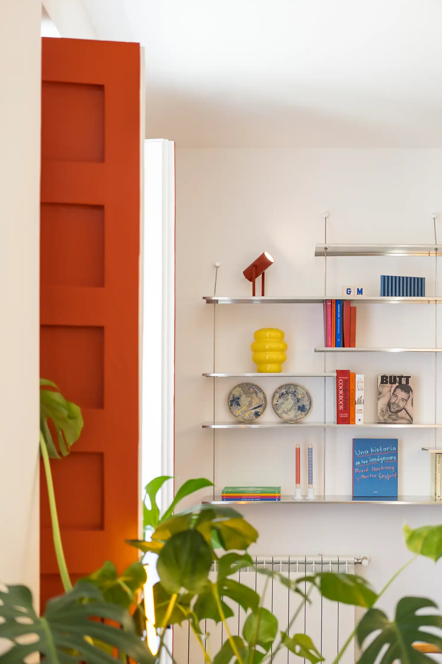 Close-up of red shutters and minimalist shelving with books and decor