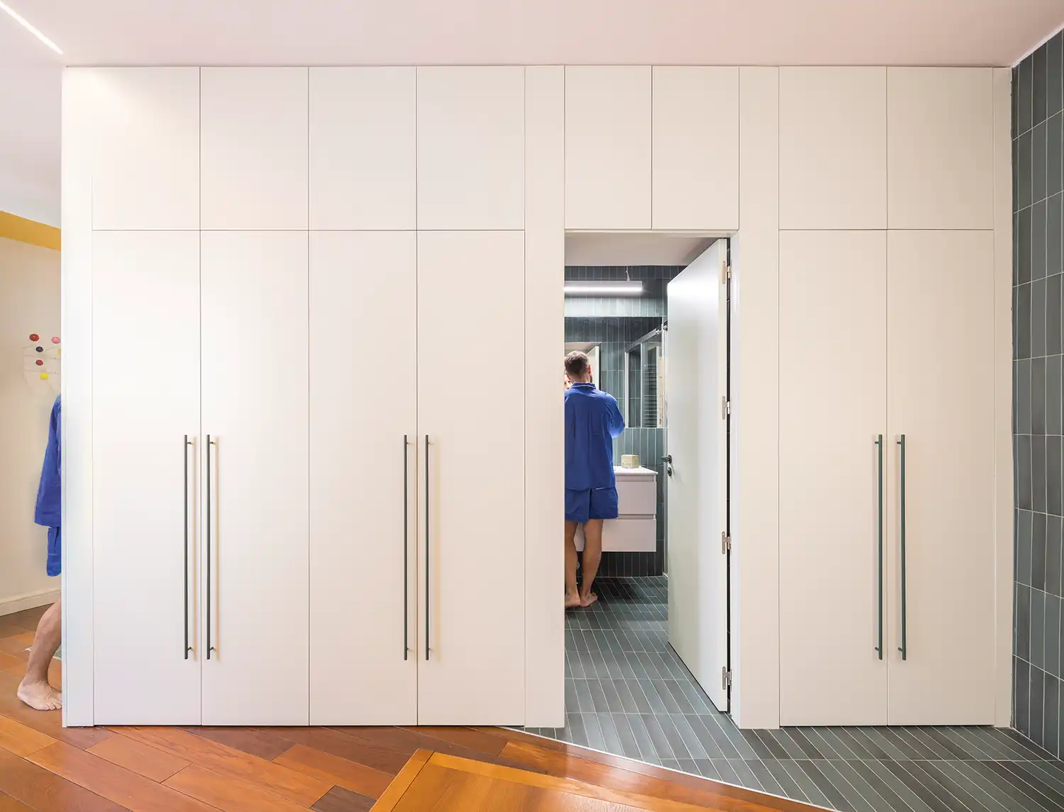 White floor-to-ceiling storage cupboards and green tiled bathroom entry