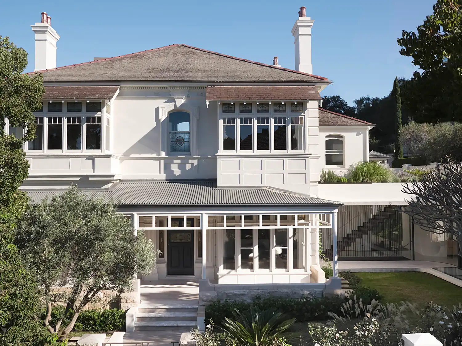 Front elevation of a white two-story Victorian heritage house with a modern glass extension in Sydney.