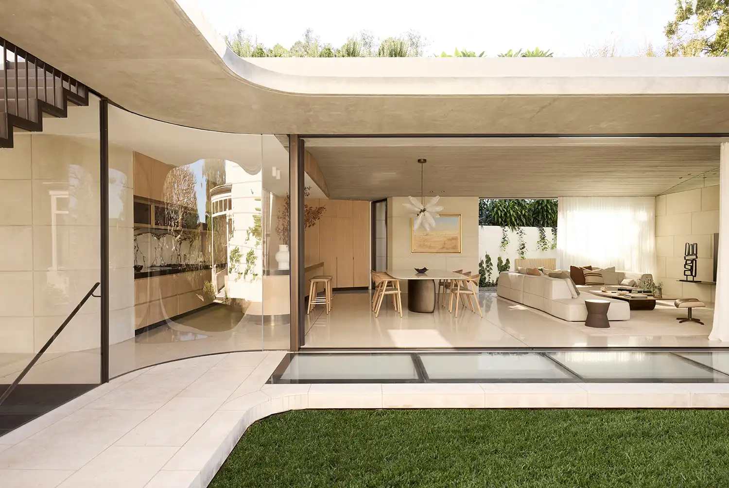 Modern glass pavilion with an open-plan living room and kitchen opening onto a green lawn and roof garden.