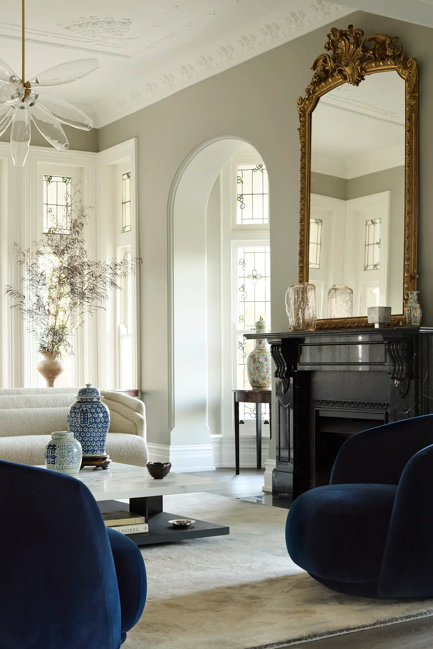 Elegant Victorian living room with a black marble fireplace, gold ornate mirror, and modern blue armchairs.