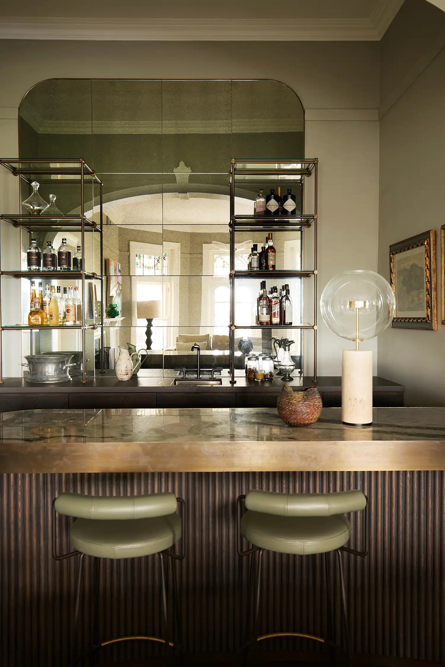 Sophisticated home bar with a brass-trimmed marble counter, fluted wood paneling, and mirrored shelving.