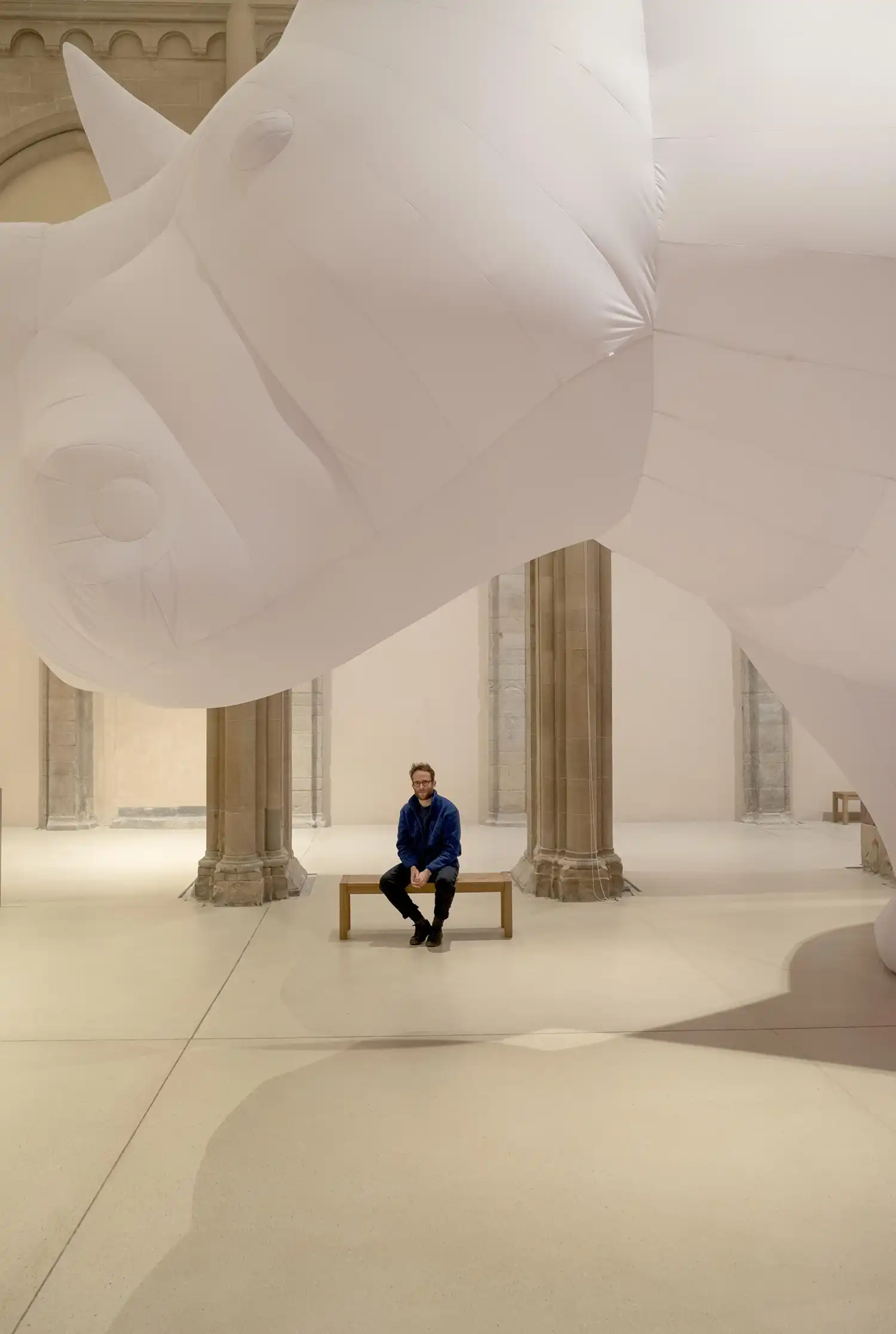 Artist Itamar Gov sitting on a bench beneath the inflatable rhinoceros
